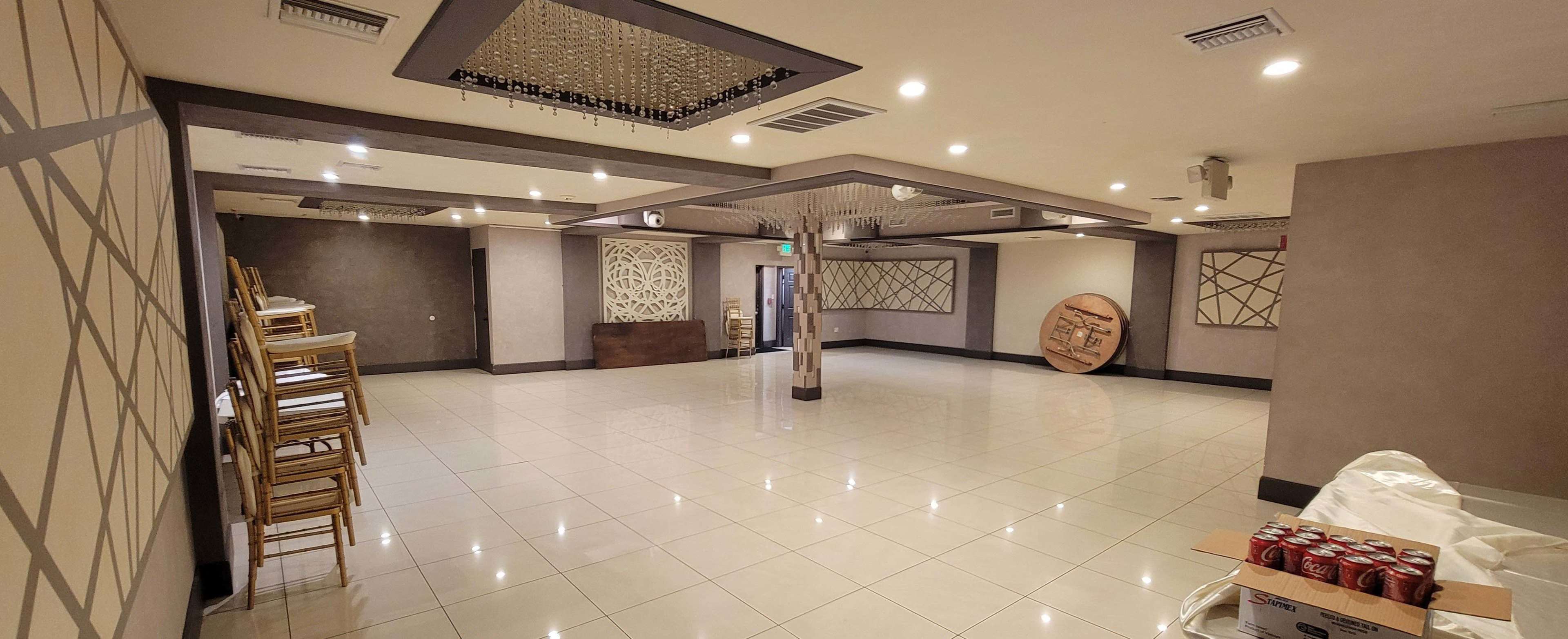 The image shows a spacious, empty event room with a polished tile floor, neatly stacked chairs against the wall, and decorative wall panels.