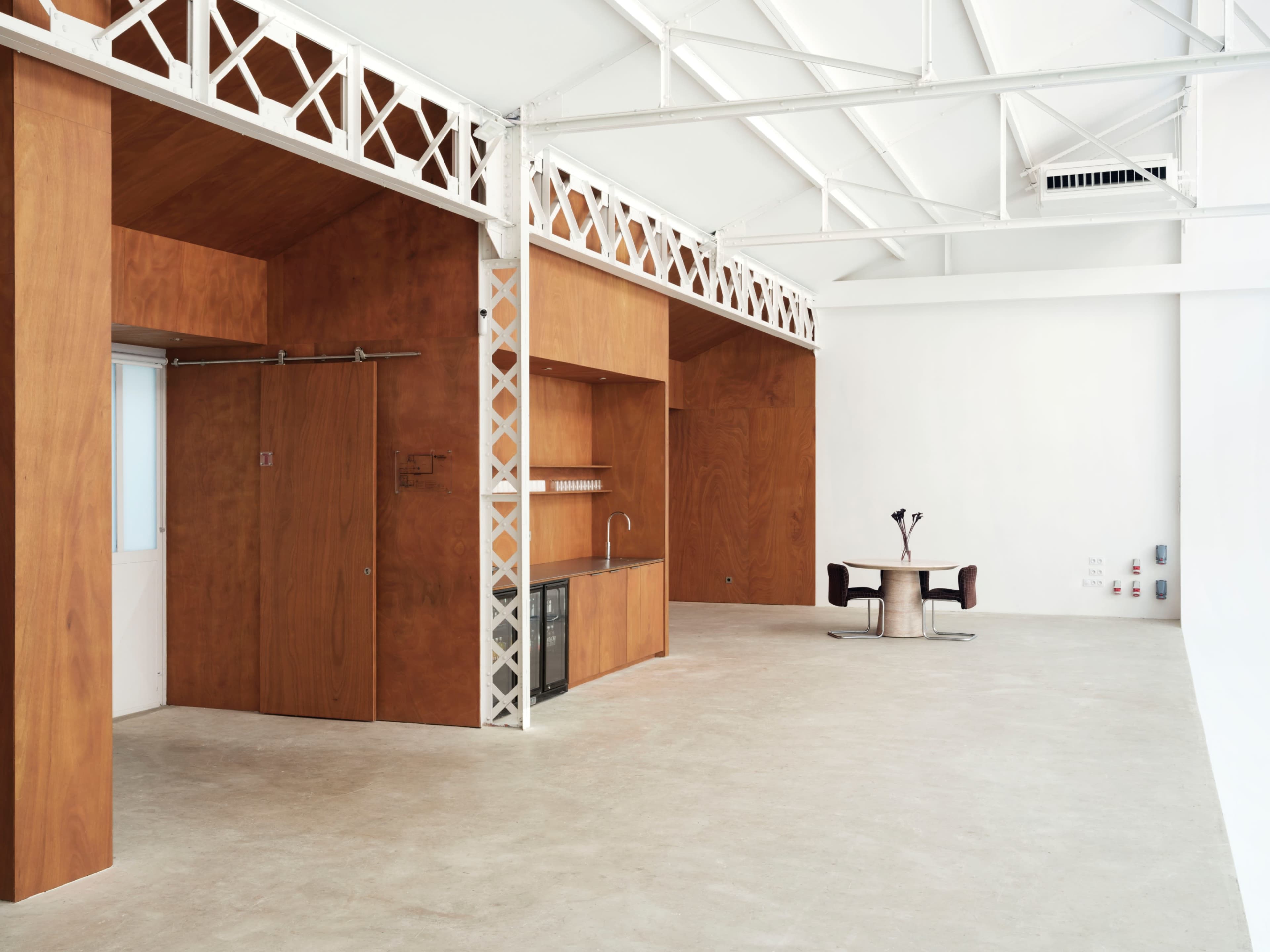 The image shows a spacious interior with wooden paneling, featuring an open kitchen area and a dining table with two chairs.