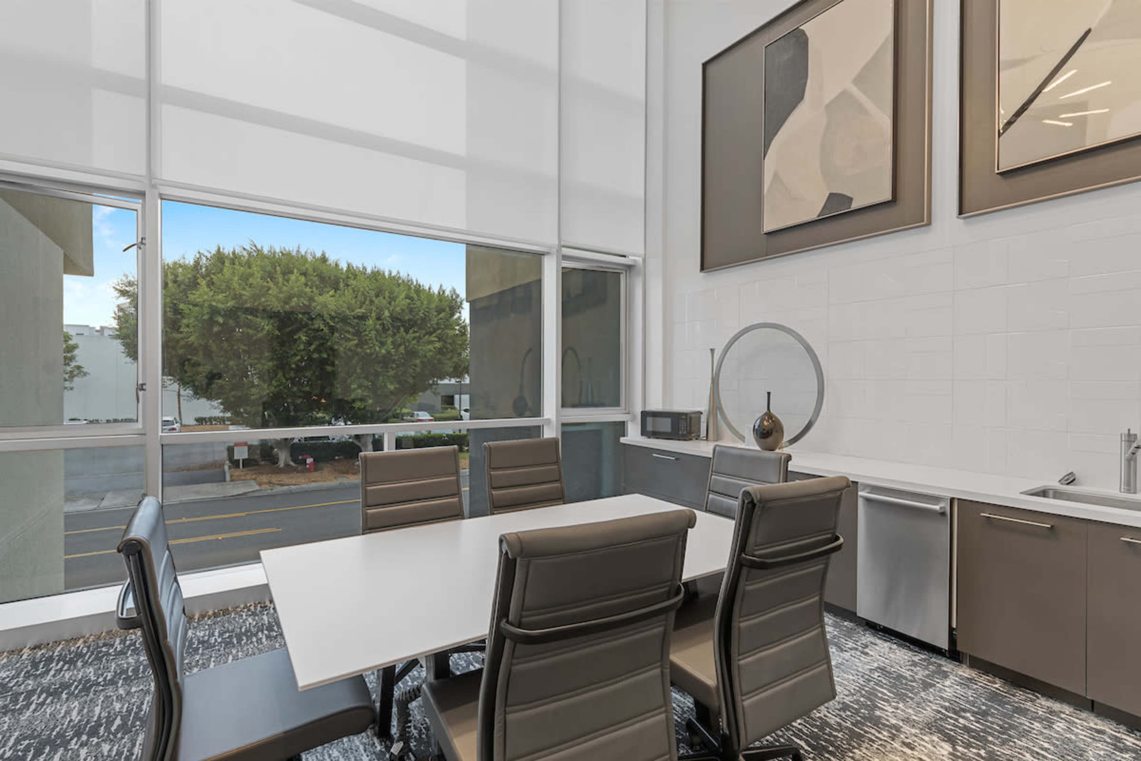 A modern conference room features a large table surrounded by leather chairs, with floor-to-ceiling windows overlooking a tree-lined street.