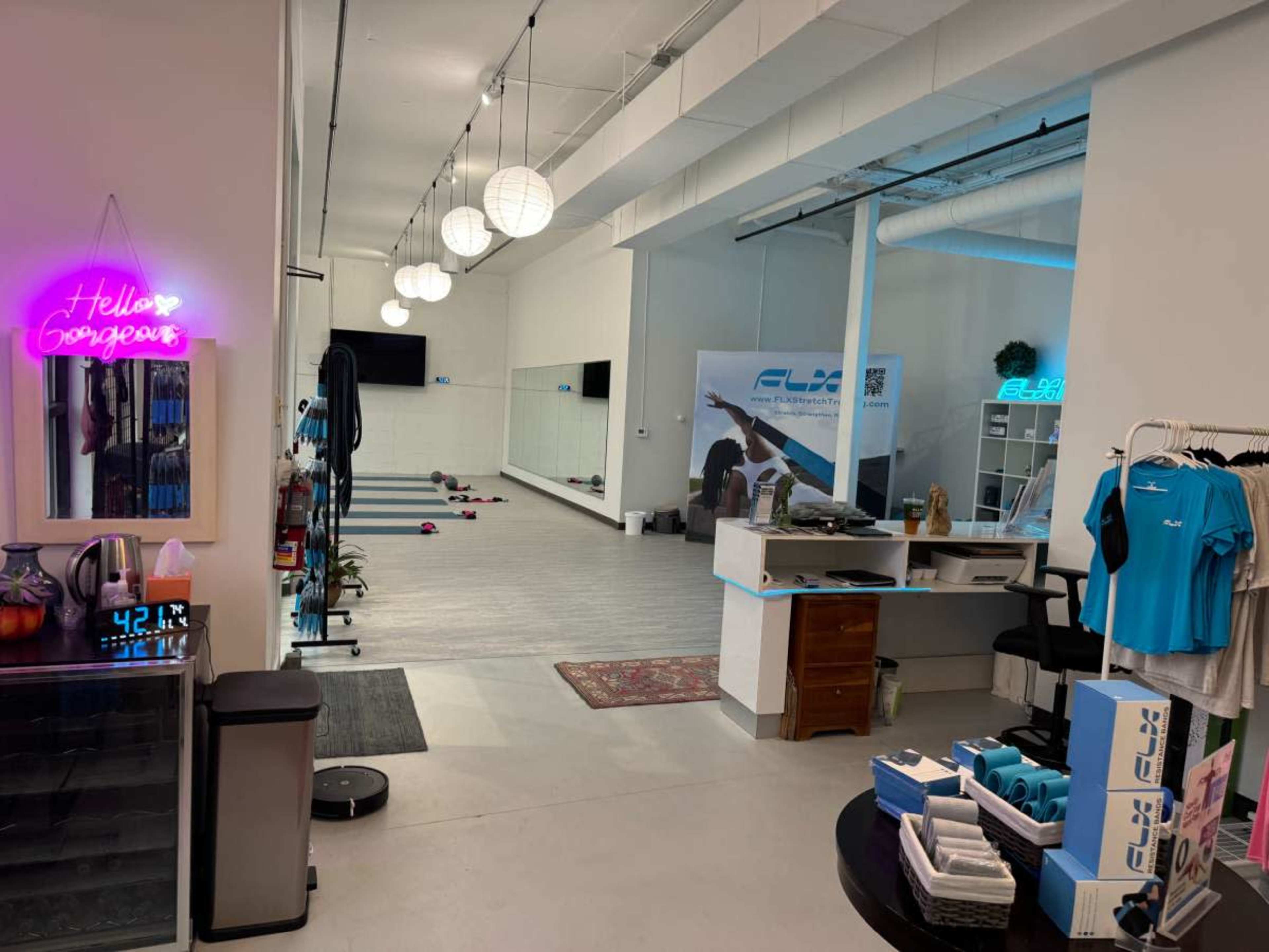 The image shows a modern fitness studio with exercise equipment, a reception area, and decorative lighting.