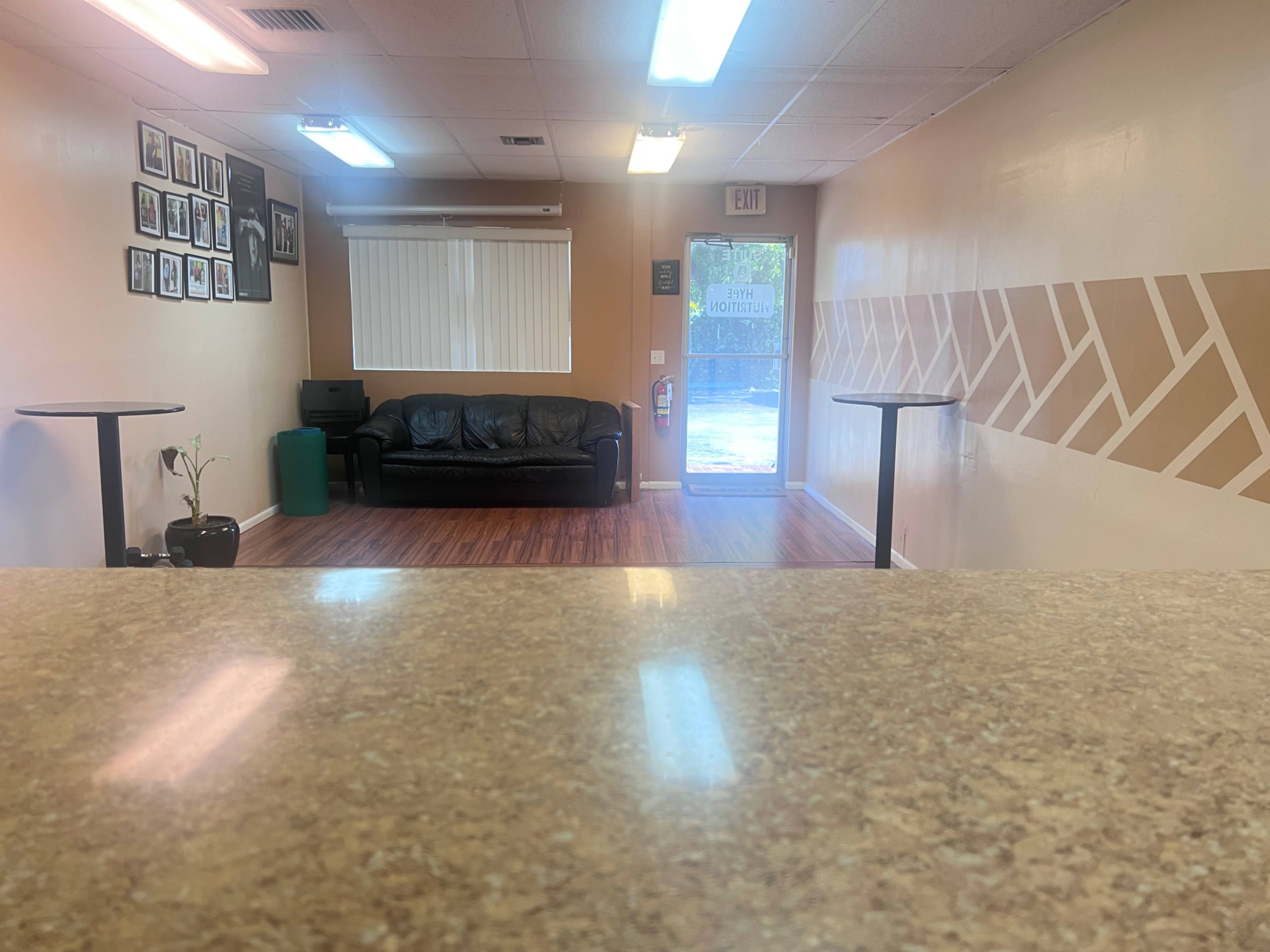 A waiting area with a black couch, two small tables, and an entrance door leading outside.