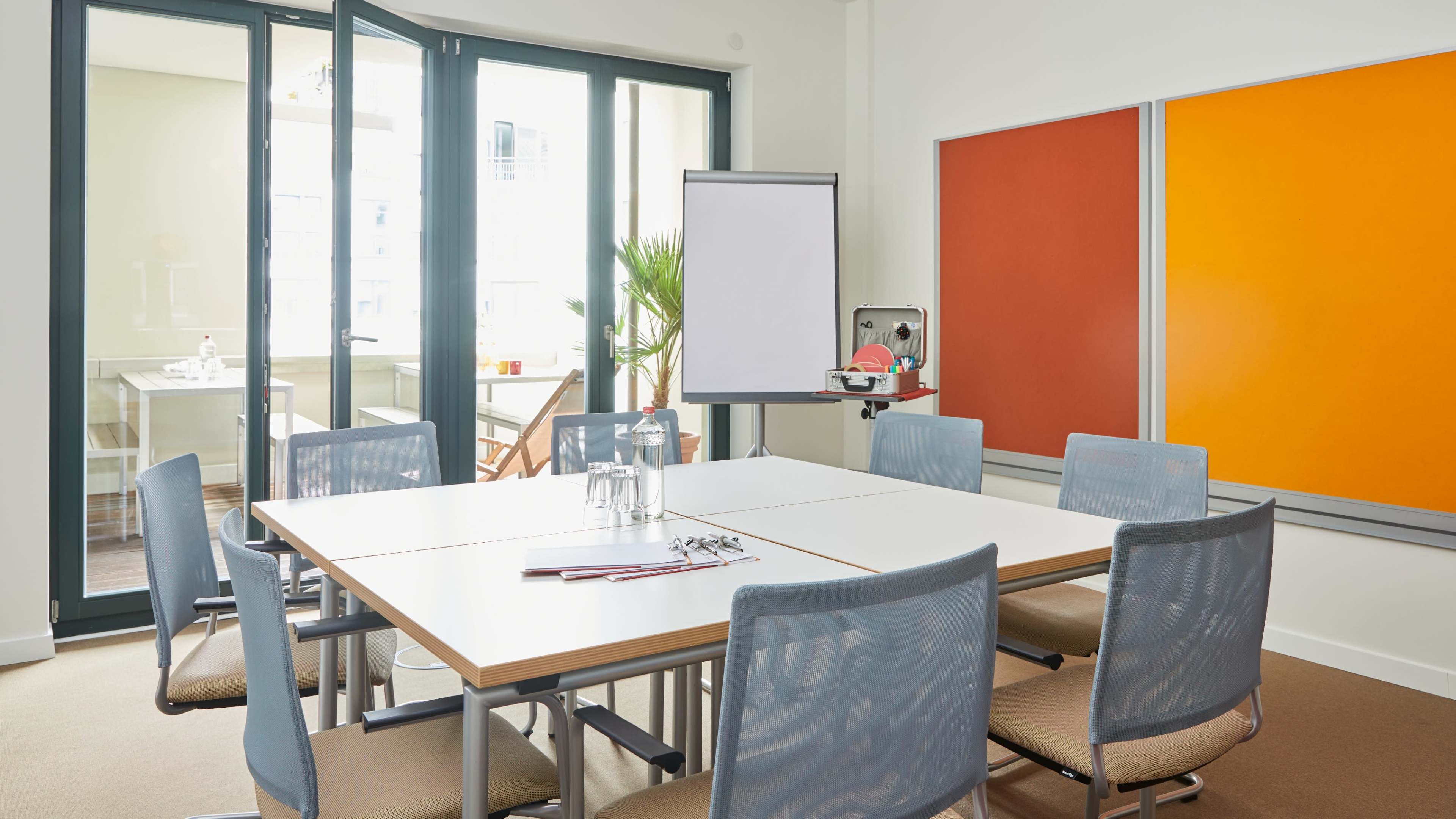 A modern conference room with a large table surrounded by chairs, featuring a whiteboard and colorful bulletin boards on the walls.