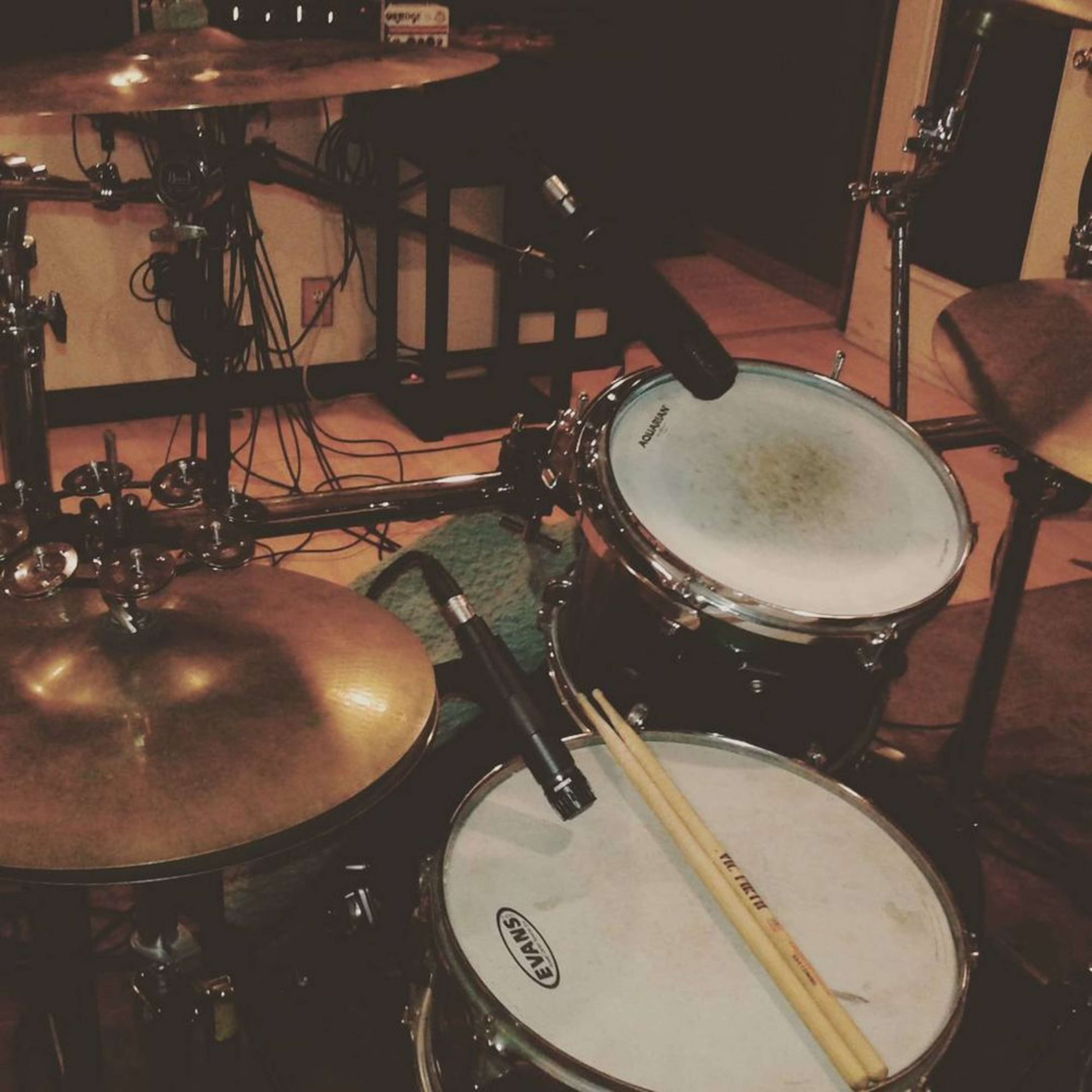 The image shows a close-up view of a drum set with microphones positioned near the drums, and a pair of drumsticks resting on the snare drum.
