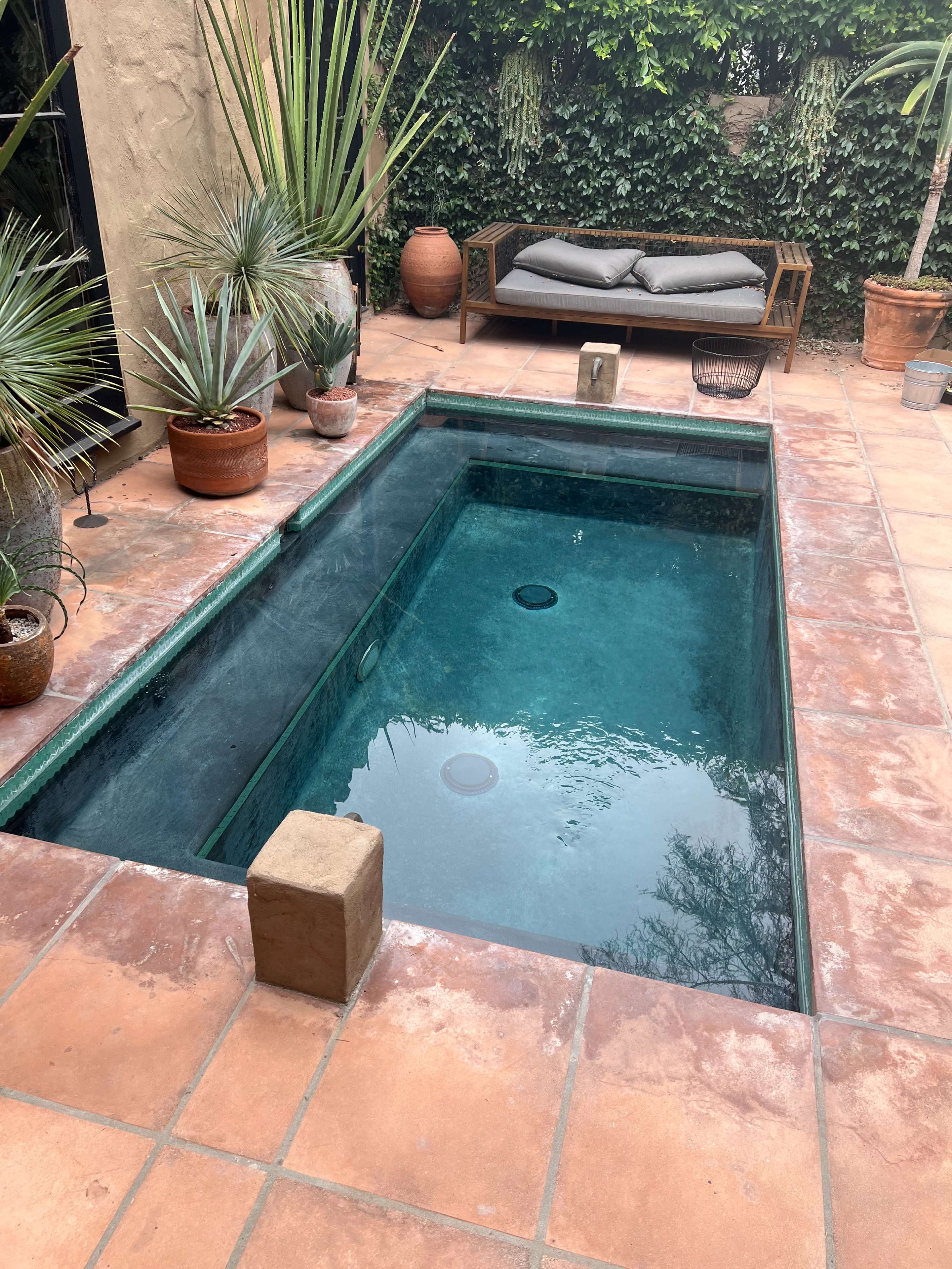 A rectangular plunge pool surrounded by potted plants and a seating area on a tiled patio.