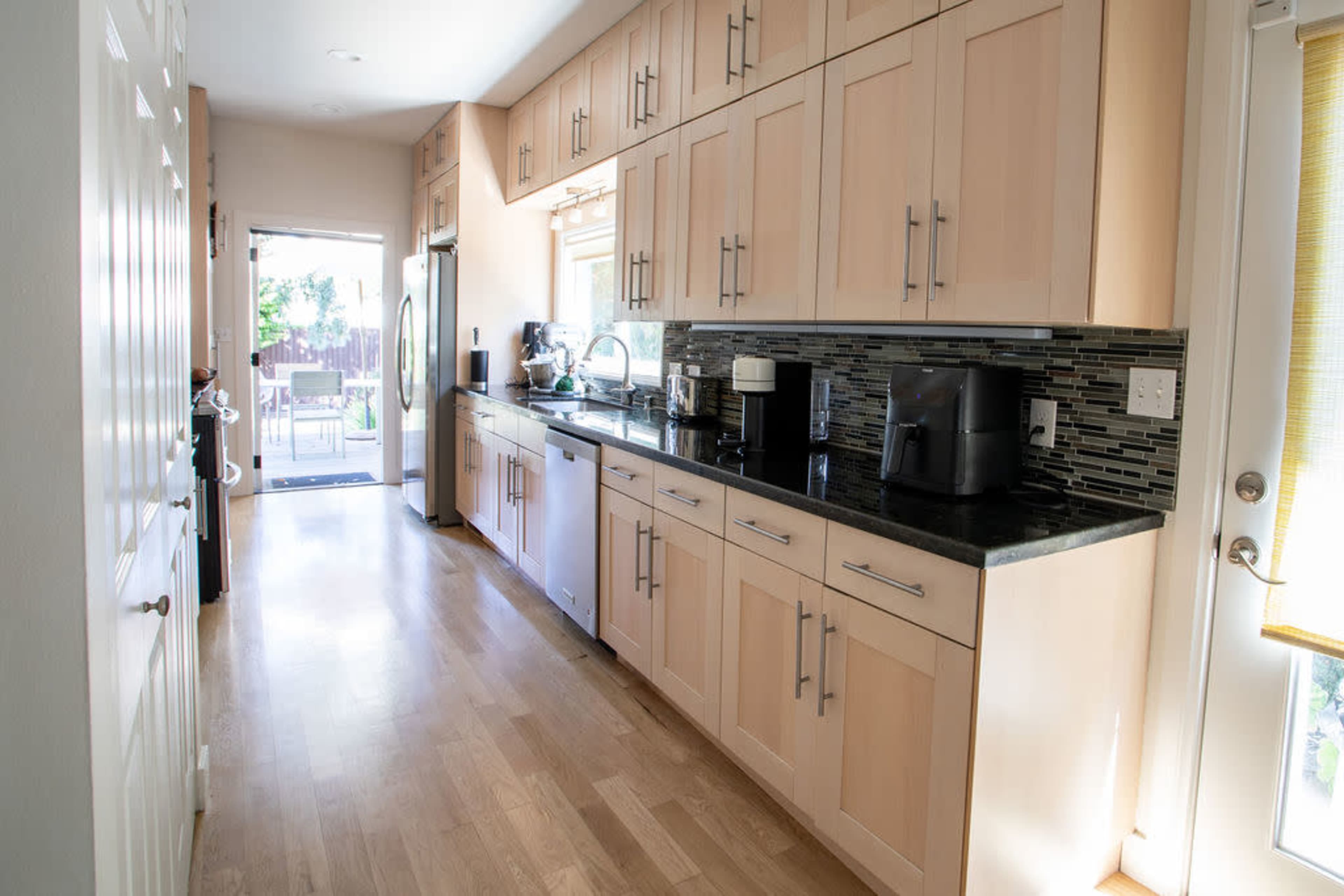 A modern kitchen featuring wooden cabinets, a dark countertop, and a door leading to an outdoor area.