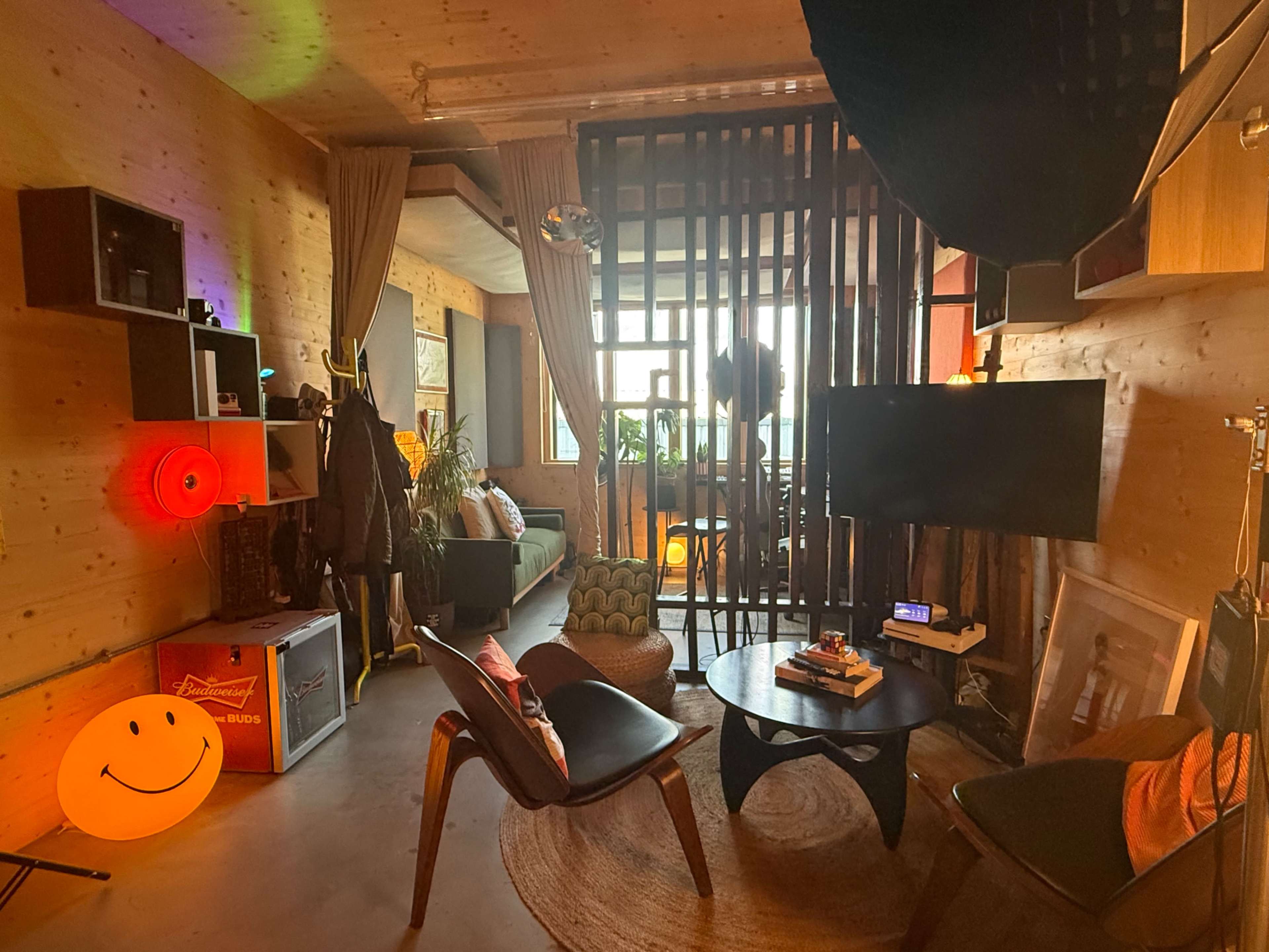 The image shows a cozy living space with wood-paneled walls, a circular rug, a small coffee table, and a mix of modern and vintage furniture.