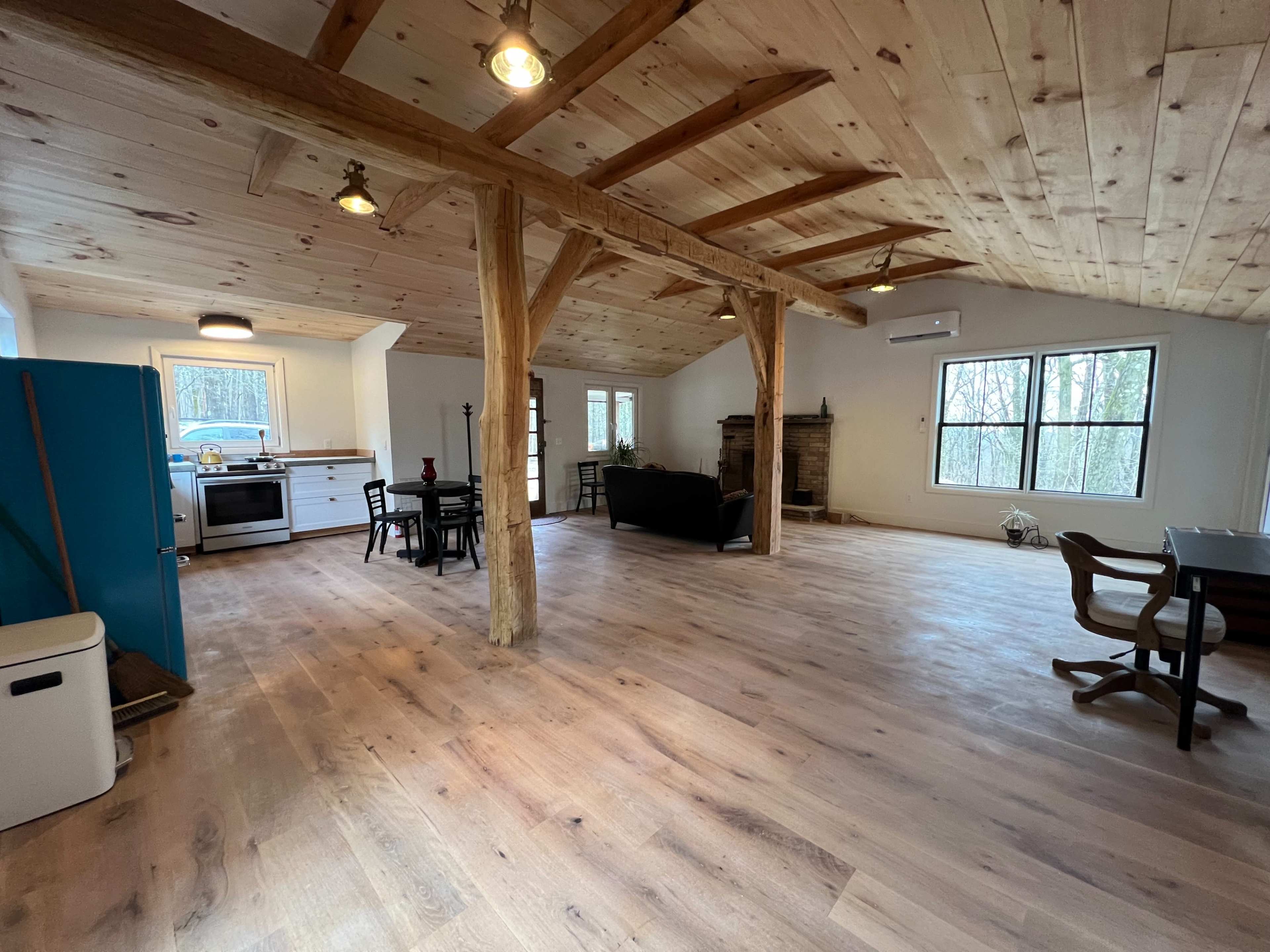 An open-concept living space with wooden beams, a kitchen area, and large windows overlooking a forested view.