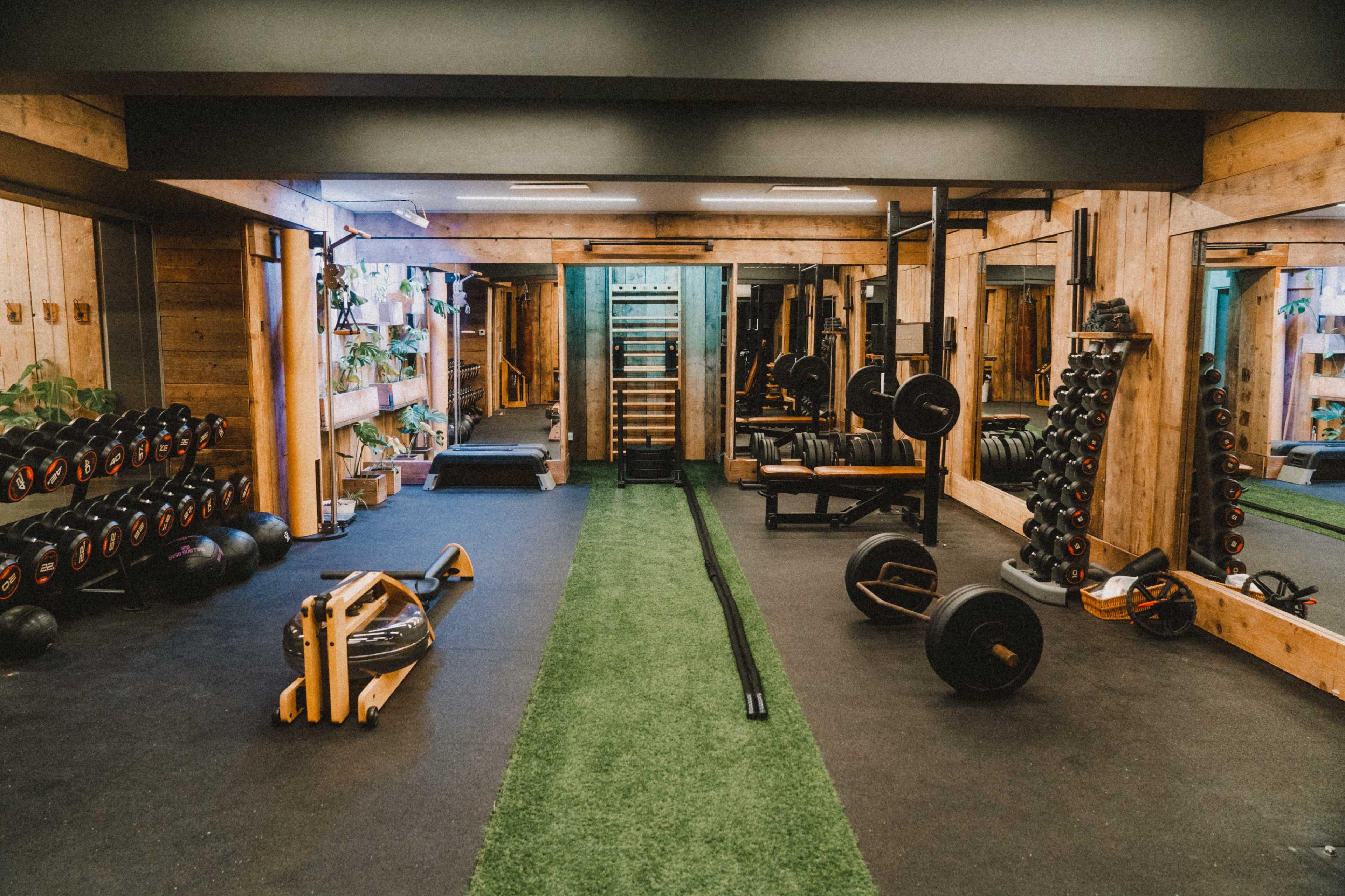 The image shows a well-equipped gym with various weights, exercise equipment, and green turf flooring.