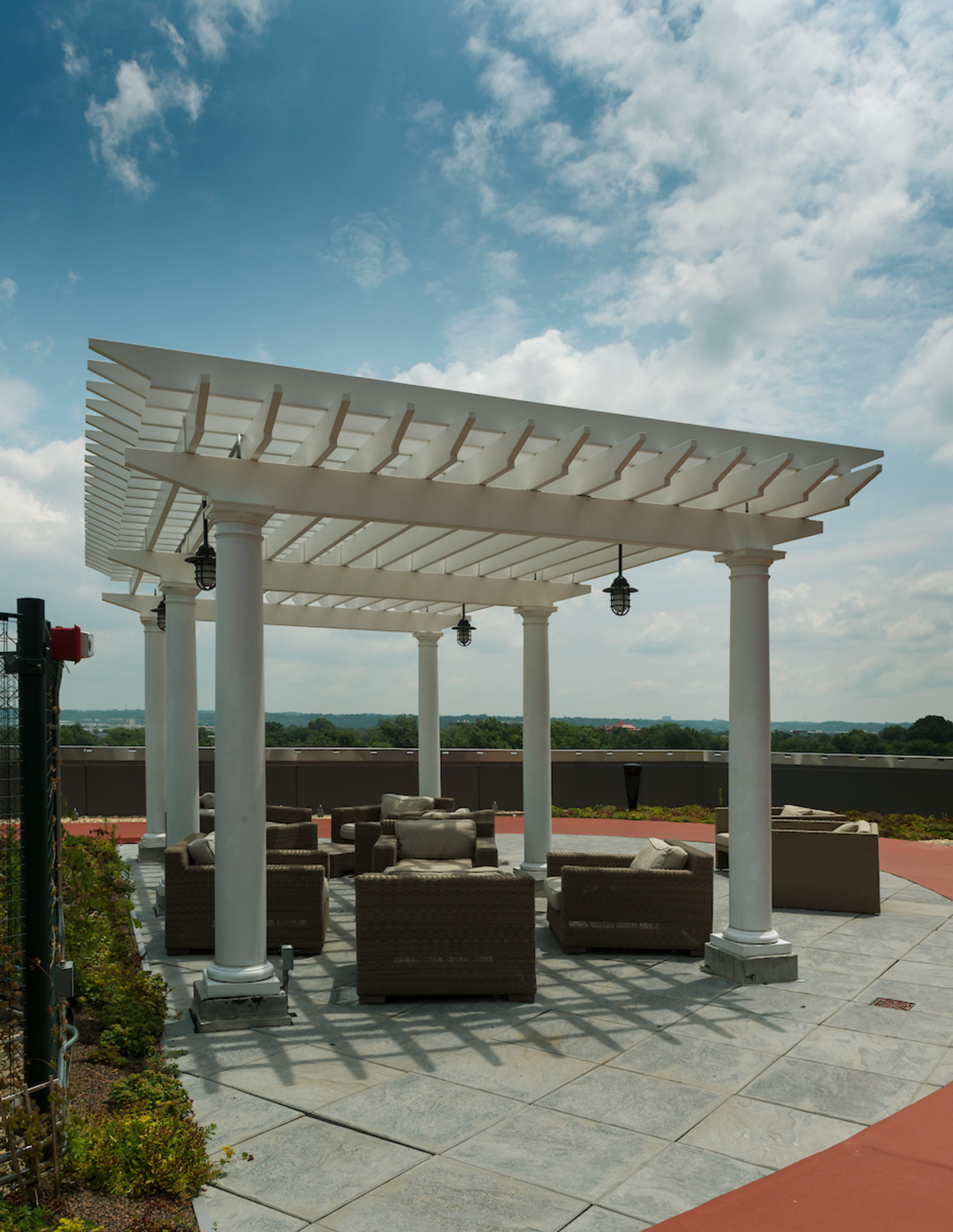 A white pergola with hanging lamps shades a seating area of wicker chairs and tables on a stone patio.