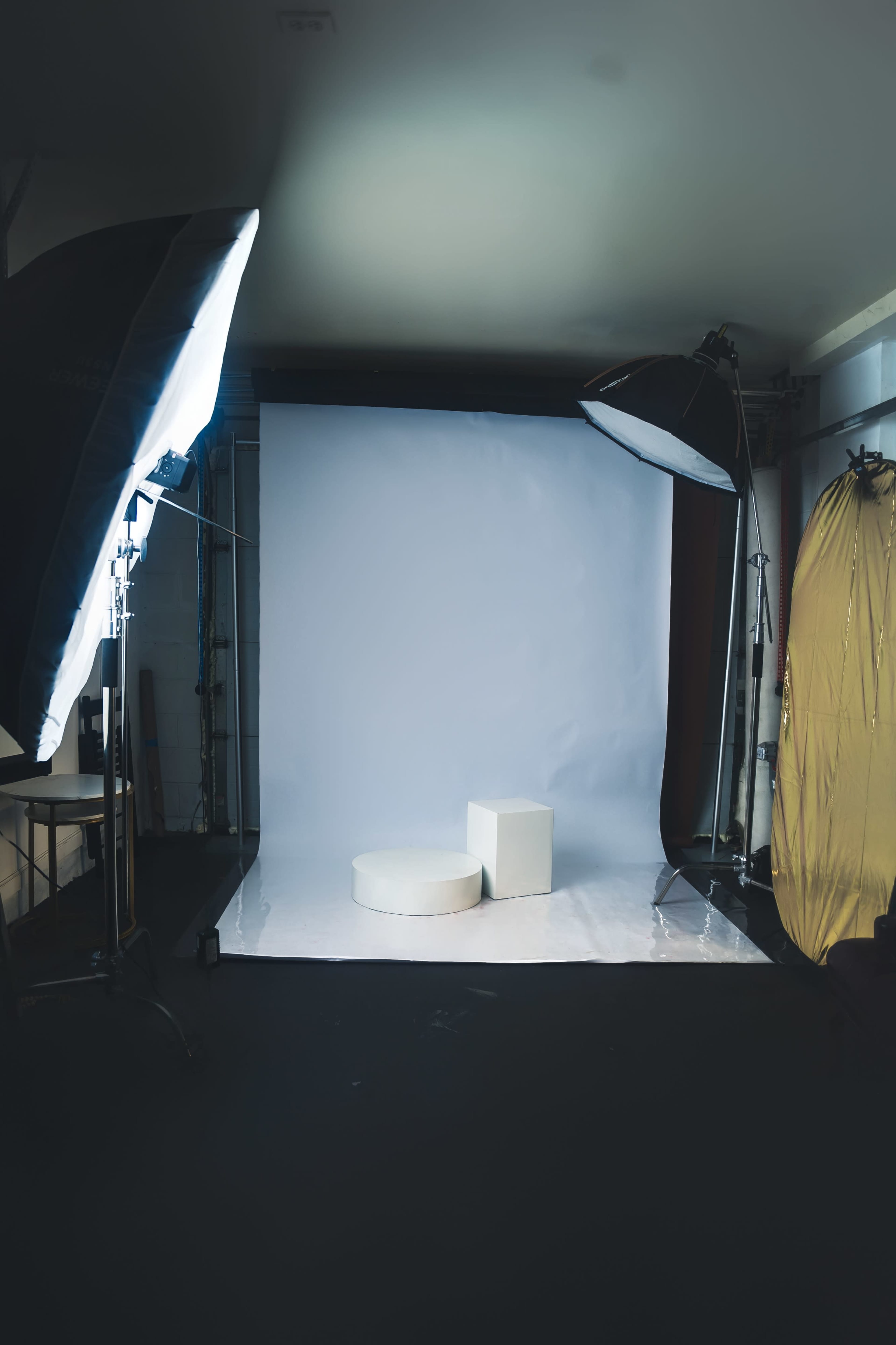The image shows a photography studio setup with two light sources, a backdrop, and two white display stands.