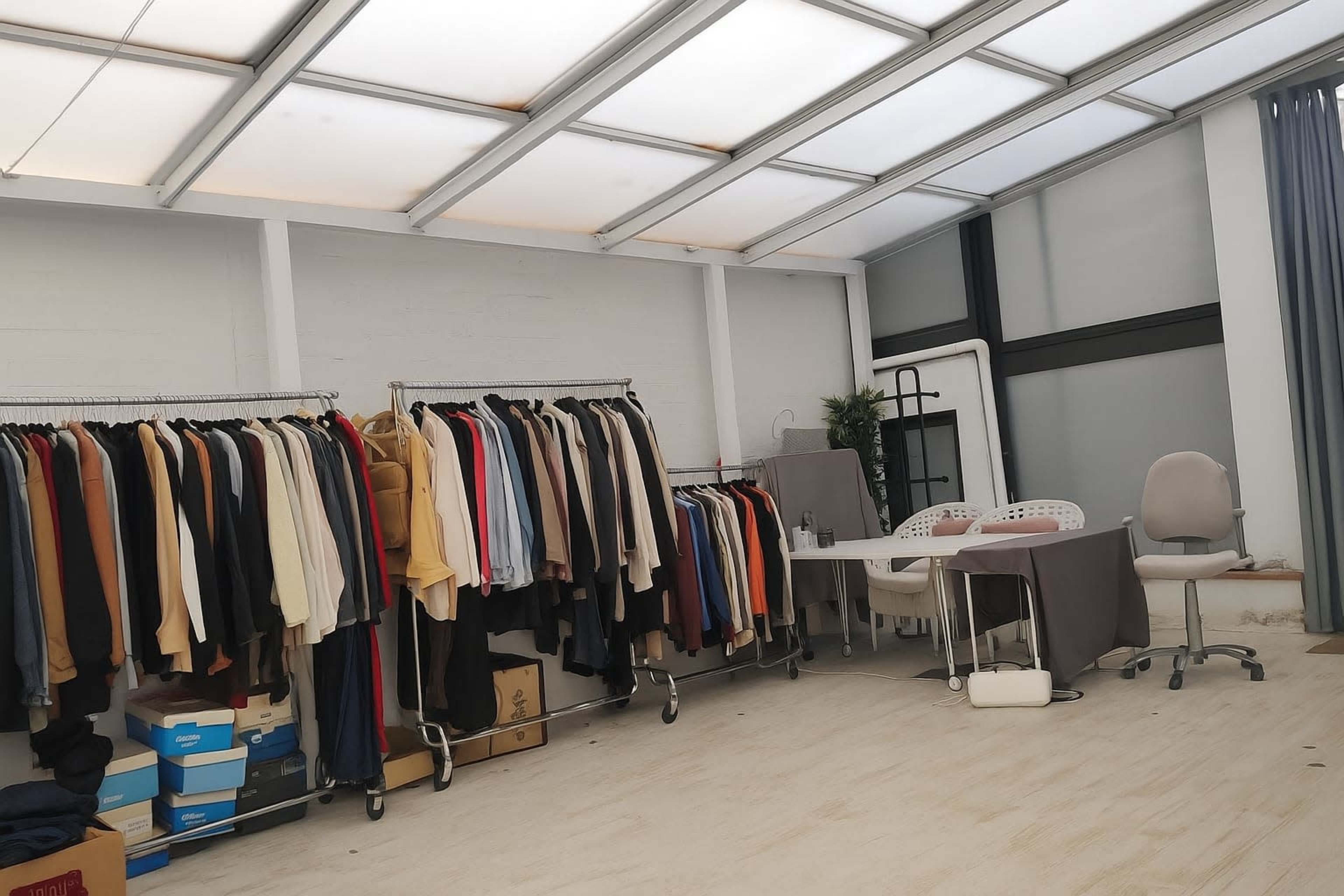 The image shows a spacious room with a rack of clothing on one side and a table with chairs on the other.