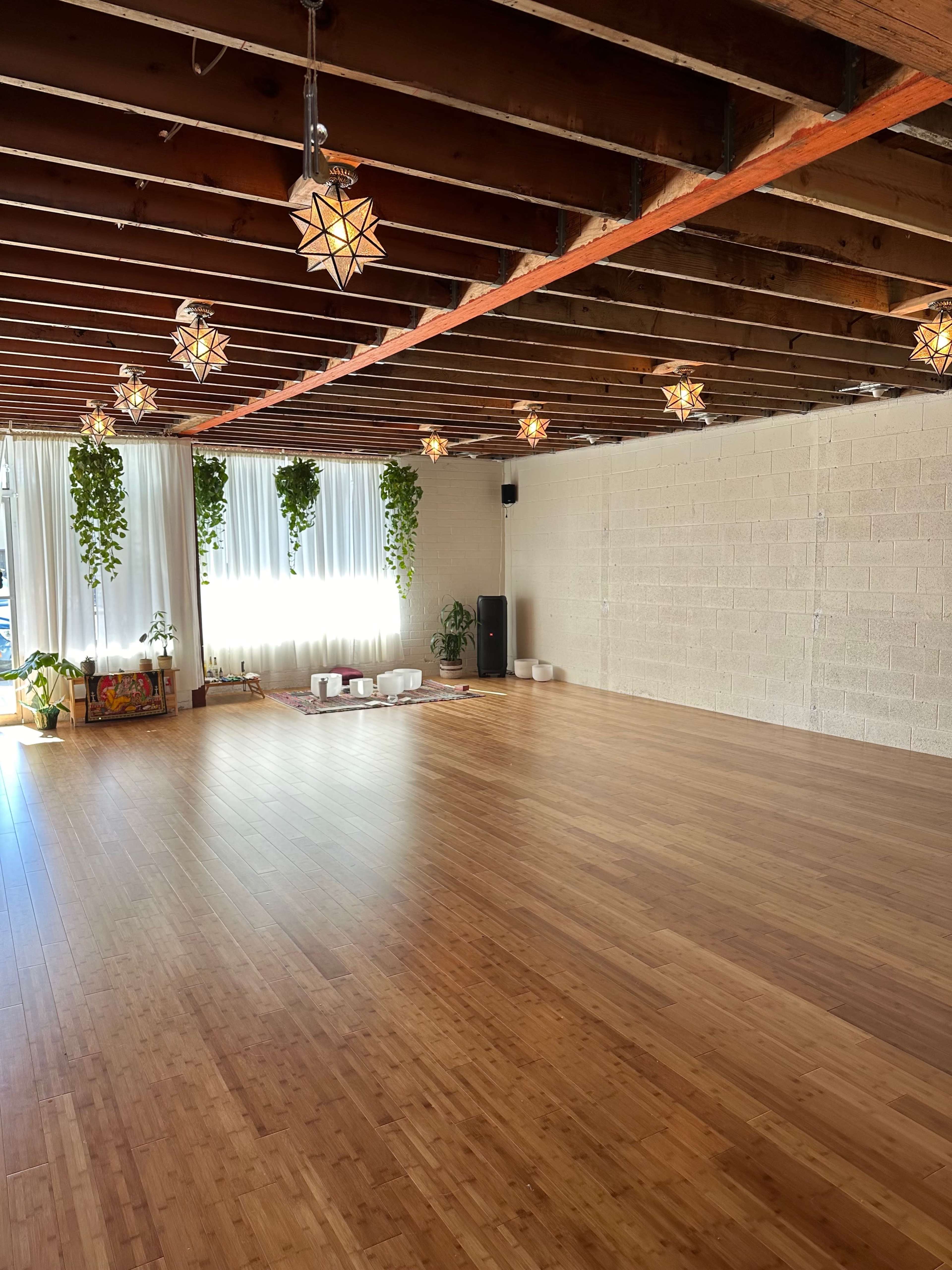 A spacious wooden yoga studio with overhead lights and plants along the walls.