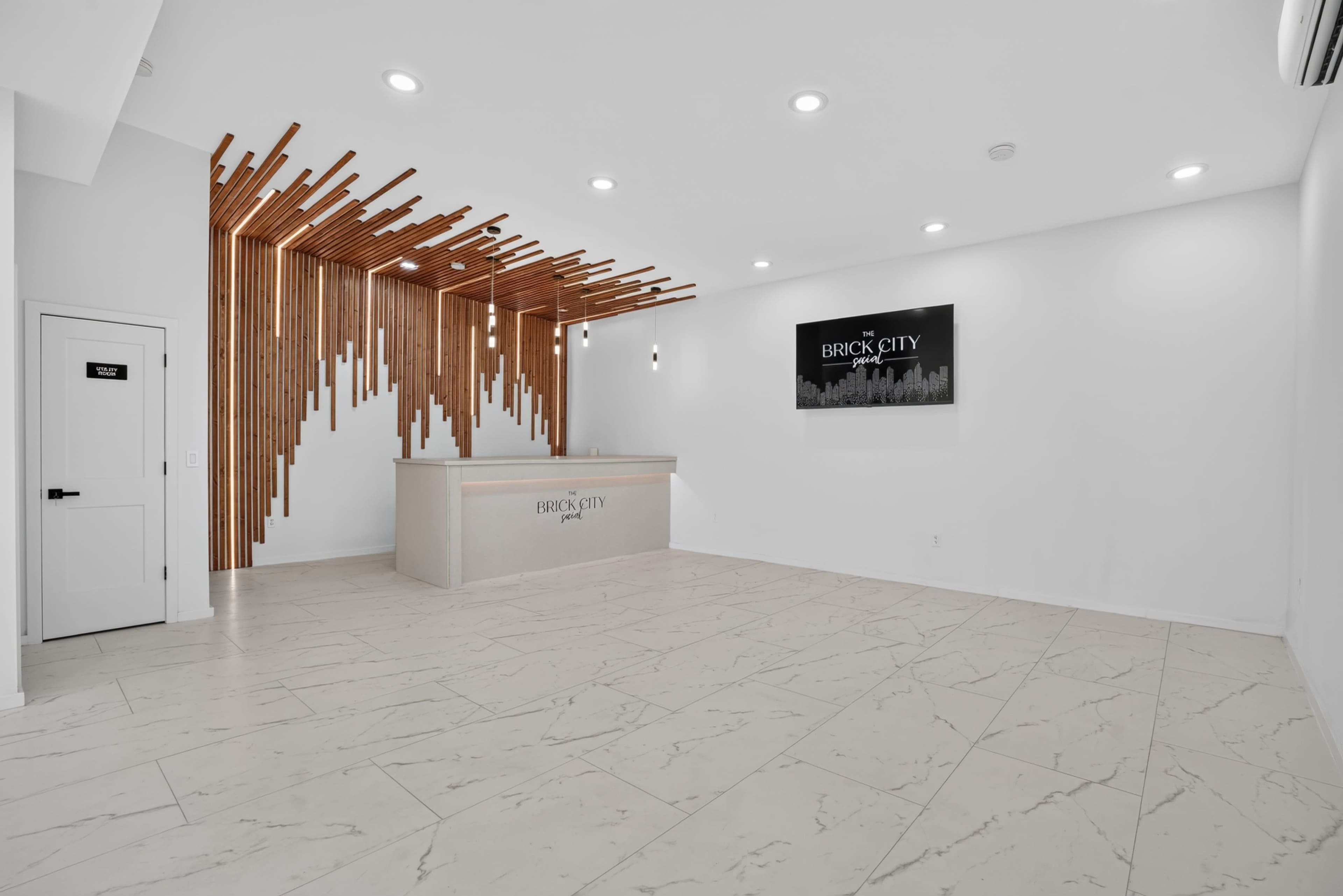 The image shows a modern reception area with a wooden feature wall, a front desk labeled "BRICK CITY," and white tile flooring.