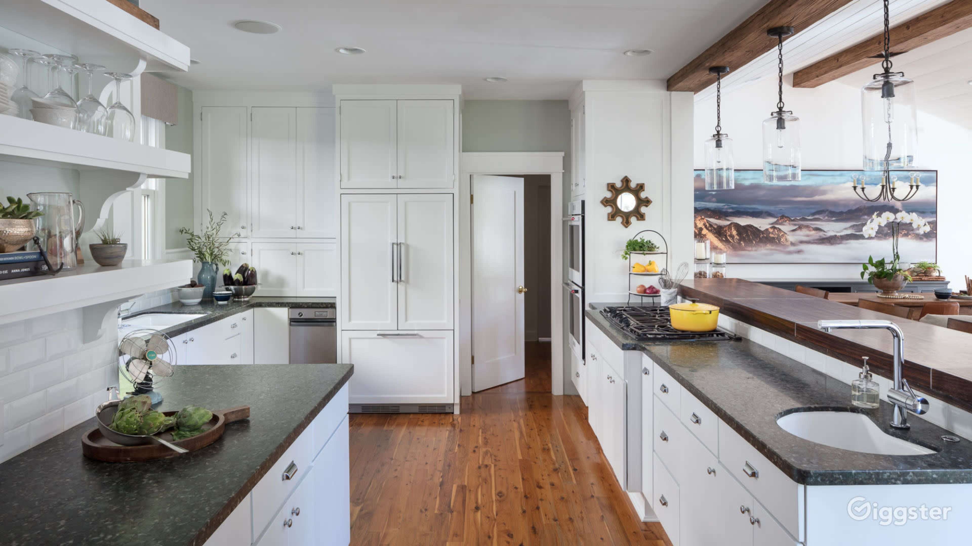 A well-organized kitchen with white cabinets, dark countertops, and a large window that offers a view of a mountain landscape.