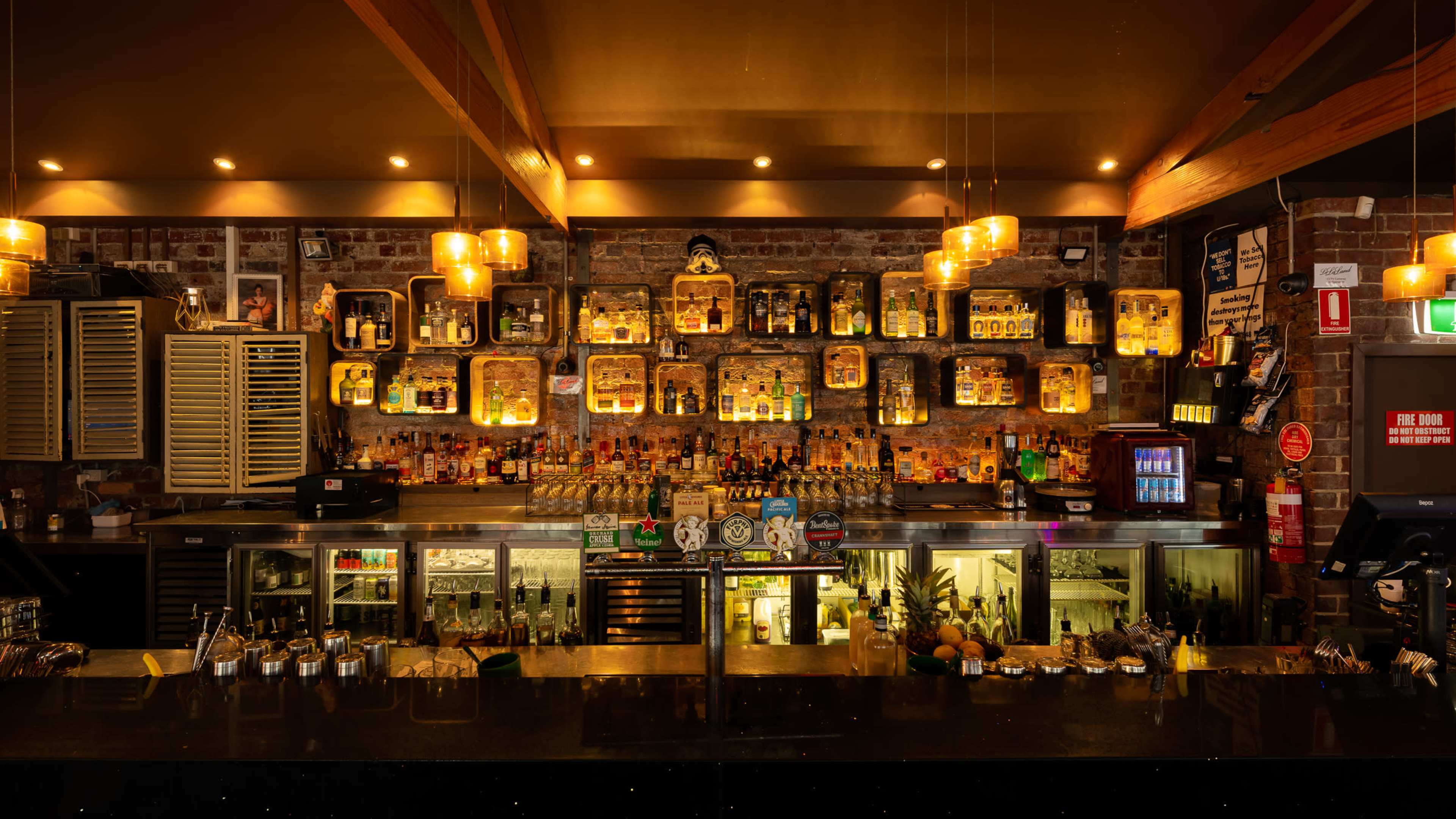 A well-lit bar with a variety of liquor bottles displayed on shelves in a brick-walled setting.