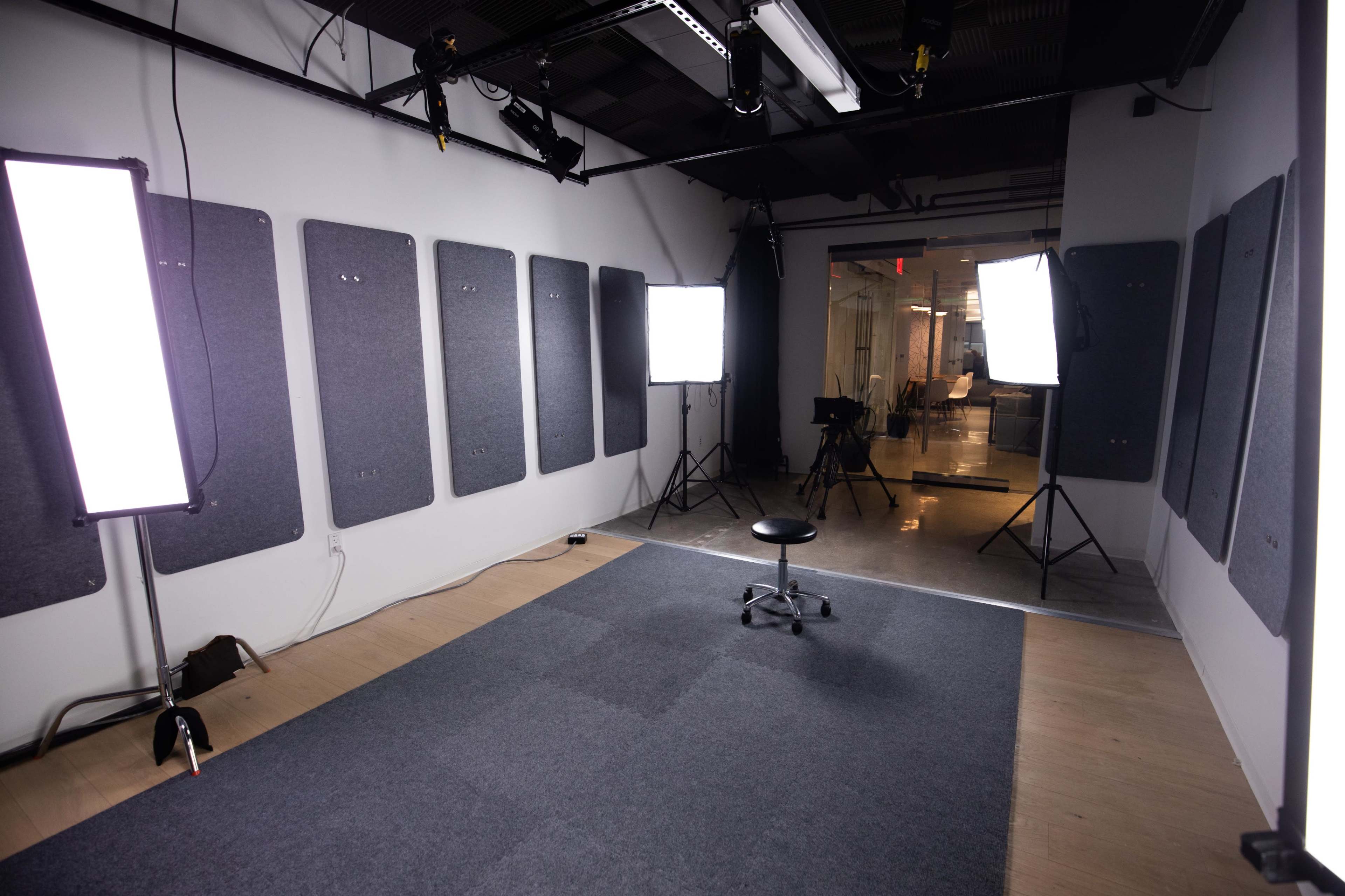 An empty studio space with soft lighting equipment set up around a central stool on a carpeted floor.