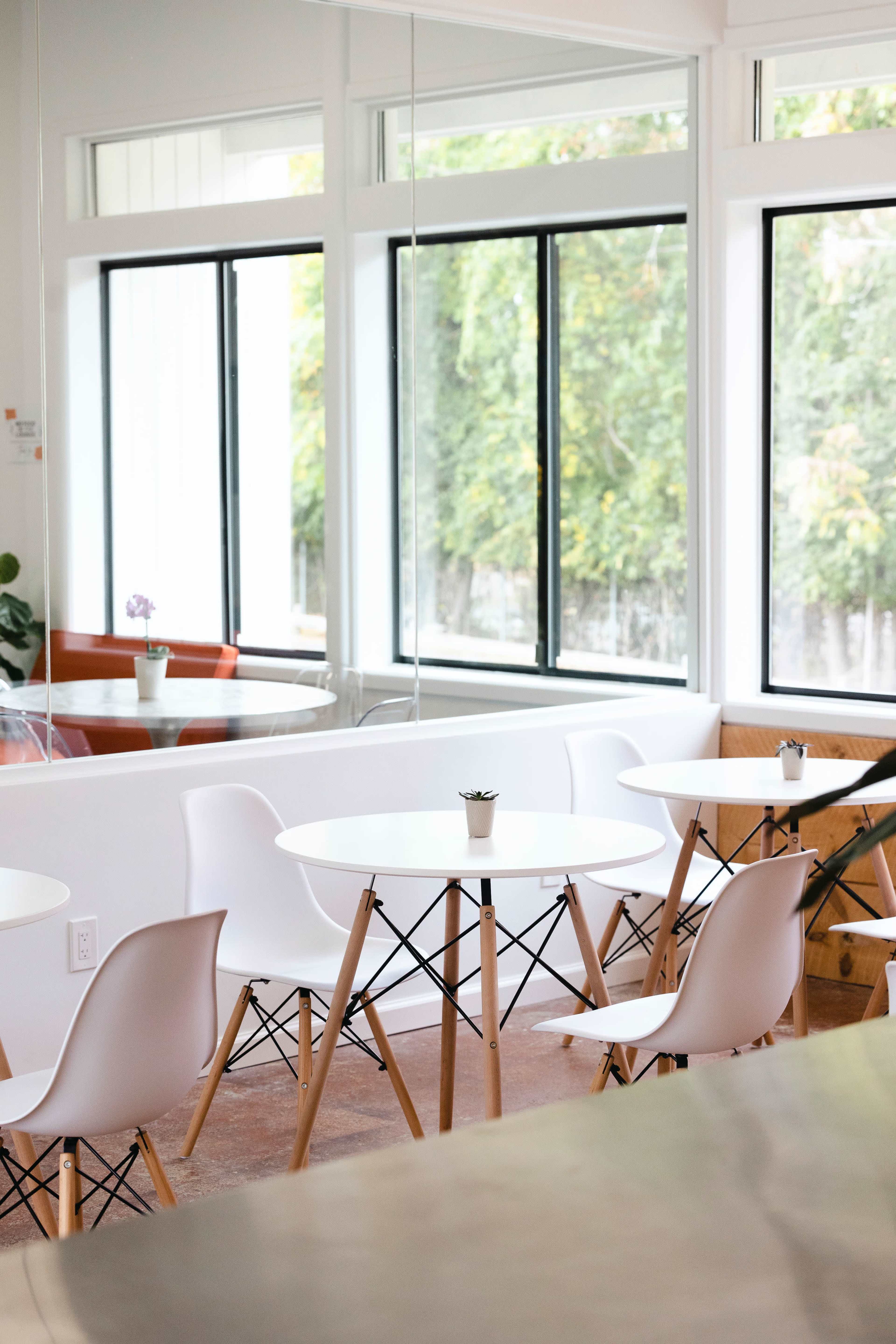 A bright café interior with several round white tables and modern chairs arranged near large windows.