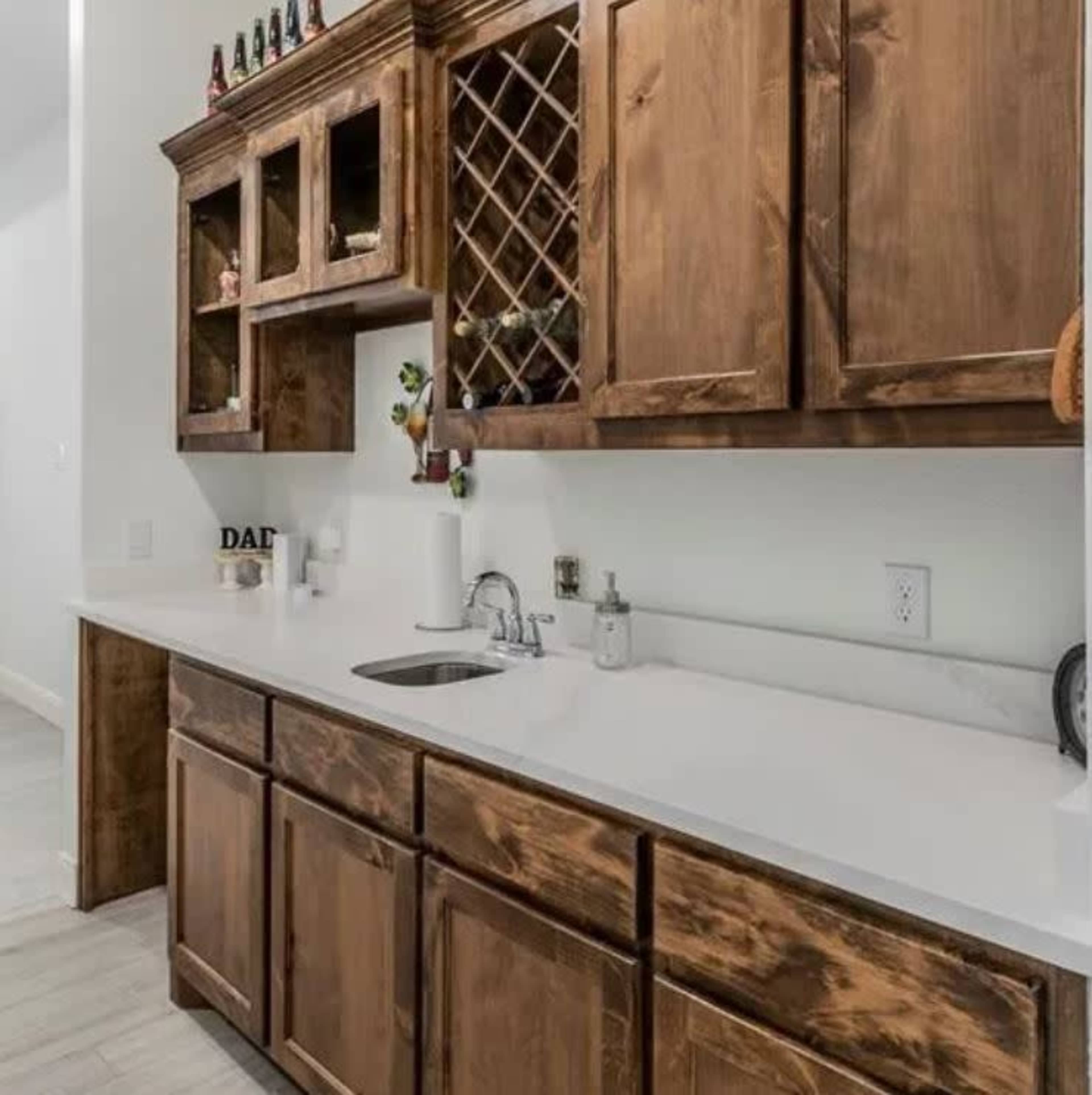 The image shows a wooden kitchen countertop with cabinets above and below, featuring a sink and a decorative wine rack.