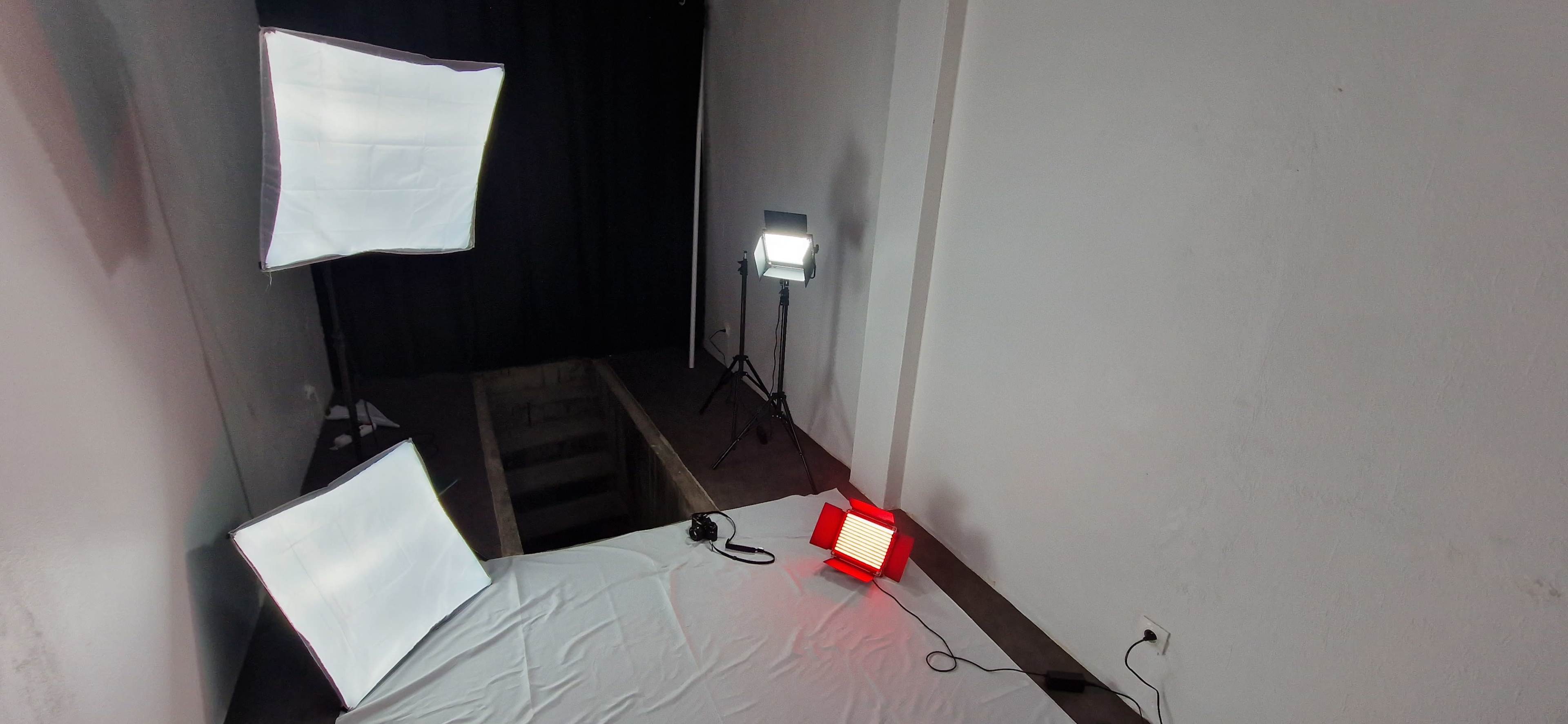 A photography setup with three lights positioned around a table covered with a white cloth in an indoor space.