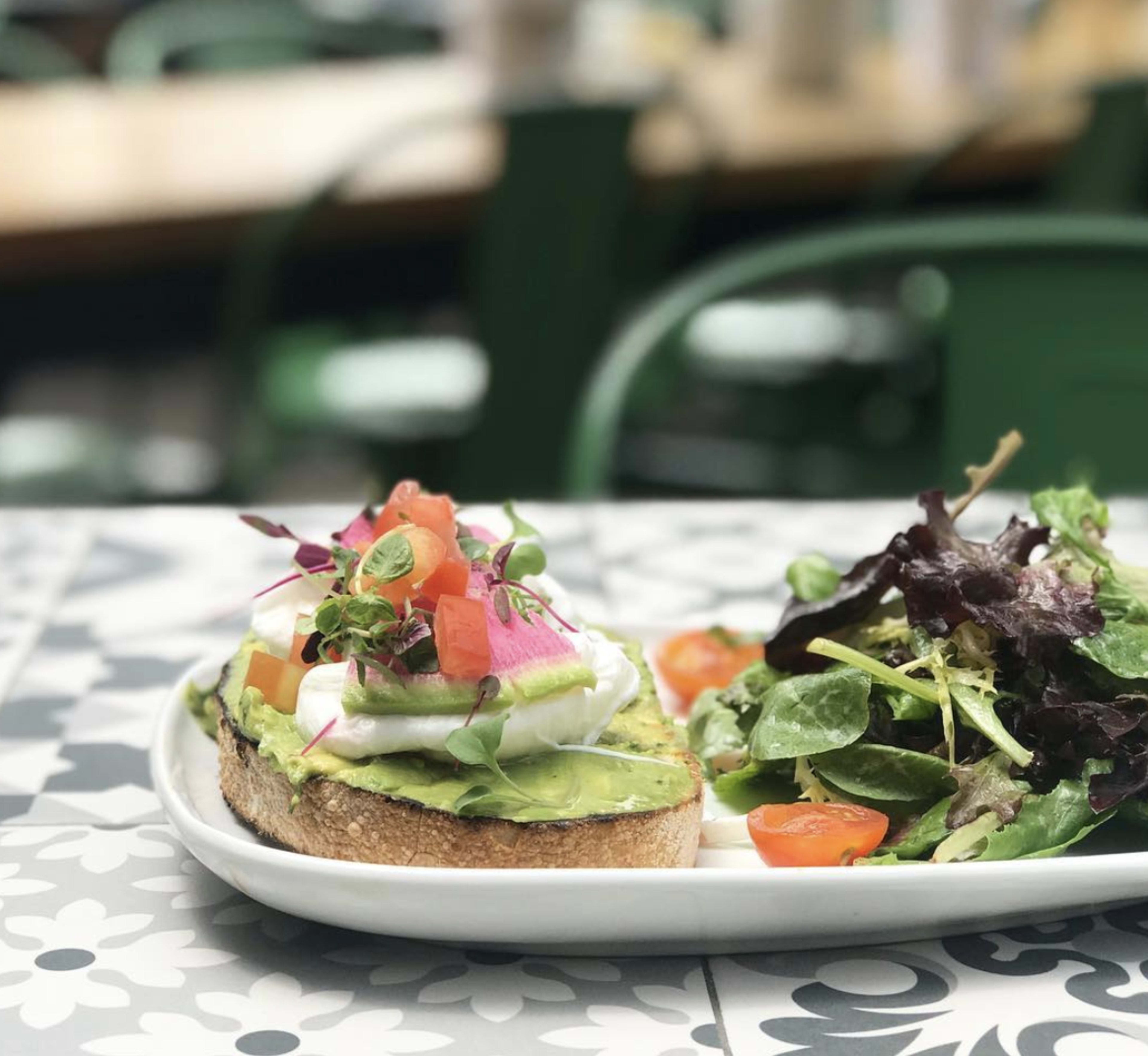 A plate featuring avocado toast topped with poached eggs and microgreens, accompanied by a side salad with mixed greens and cherry tomatoes.