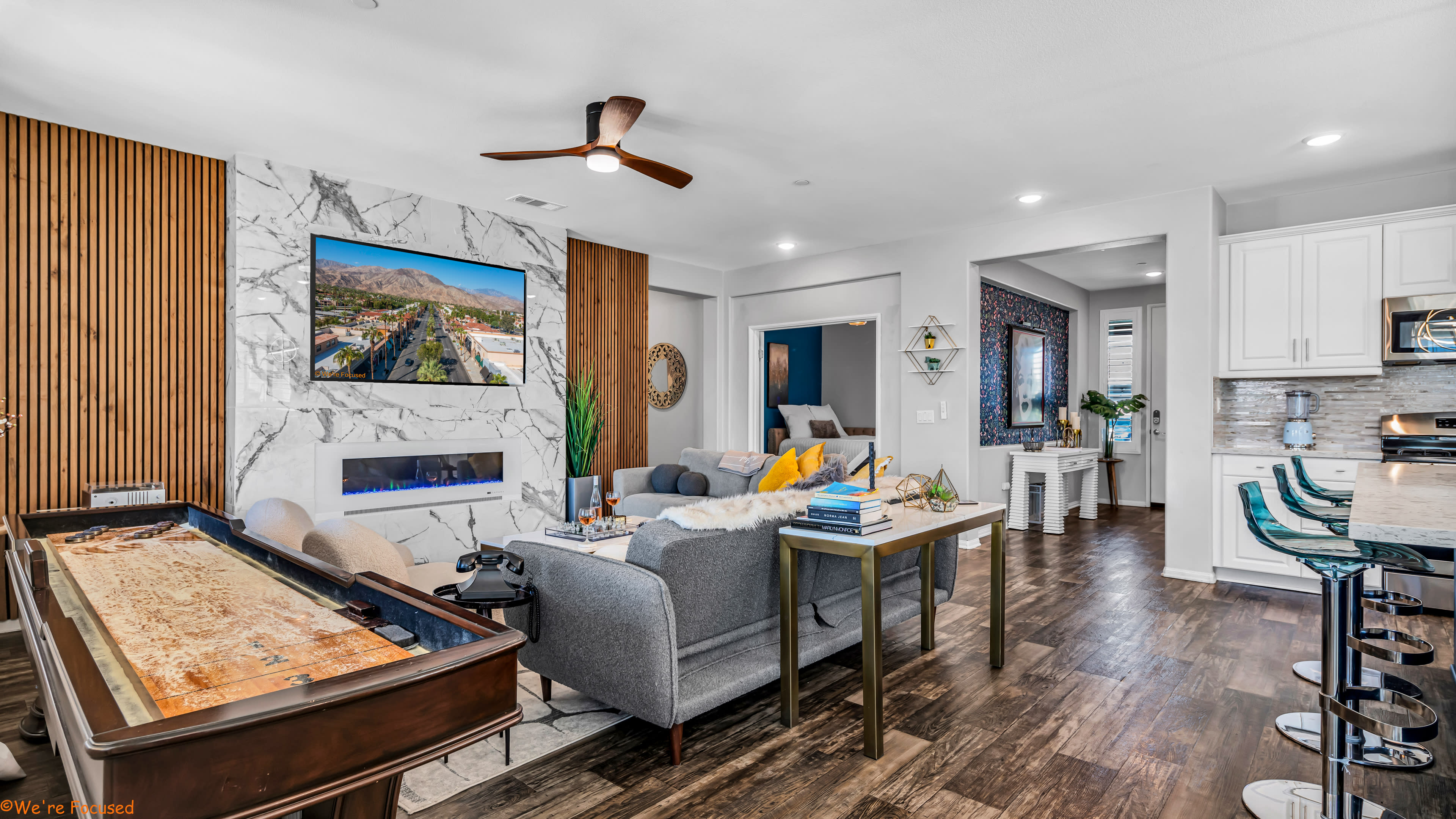 The living room features a marble accent wall, a ceiling fan, a large television mounted above a modern fireplace, and a sectional sofa with various decorative pillows.