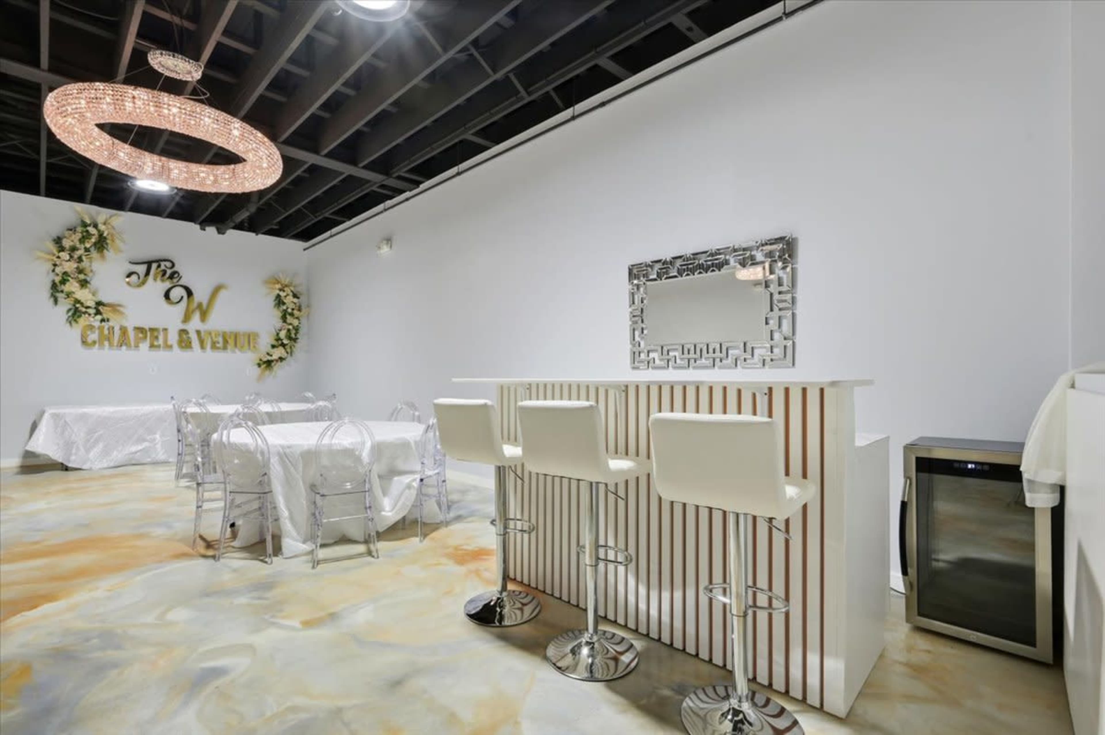The image shows a modern event space with a bar area, a table set for dining, and decorative floral elements on the wall.