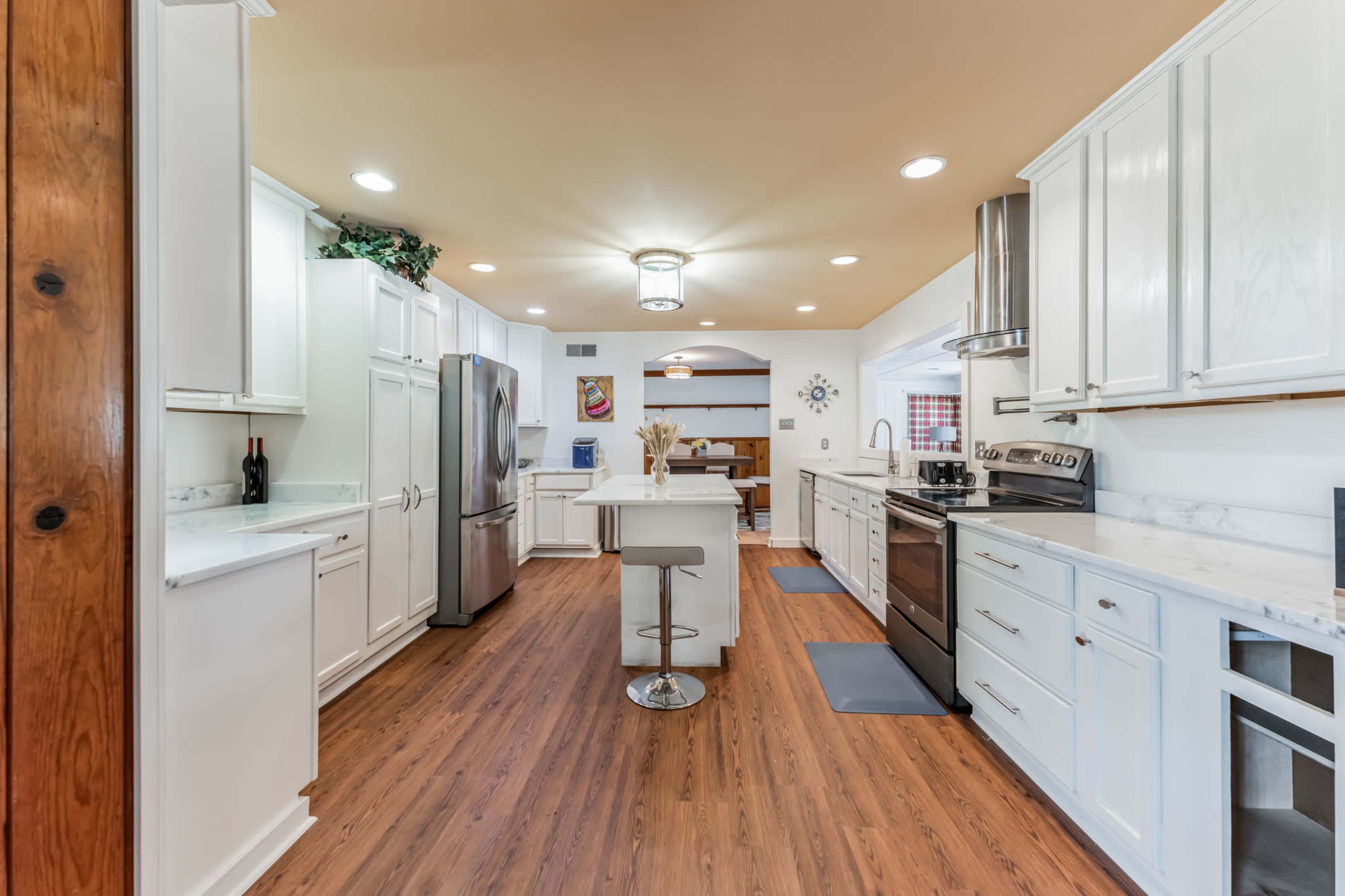 A modern kitchen featuring white cabinetry, stainless steel appliances, and a central island with a stool, all set against a wood-paneled wall and warm-toned flooring.