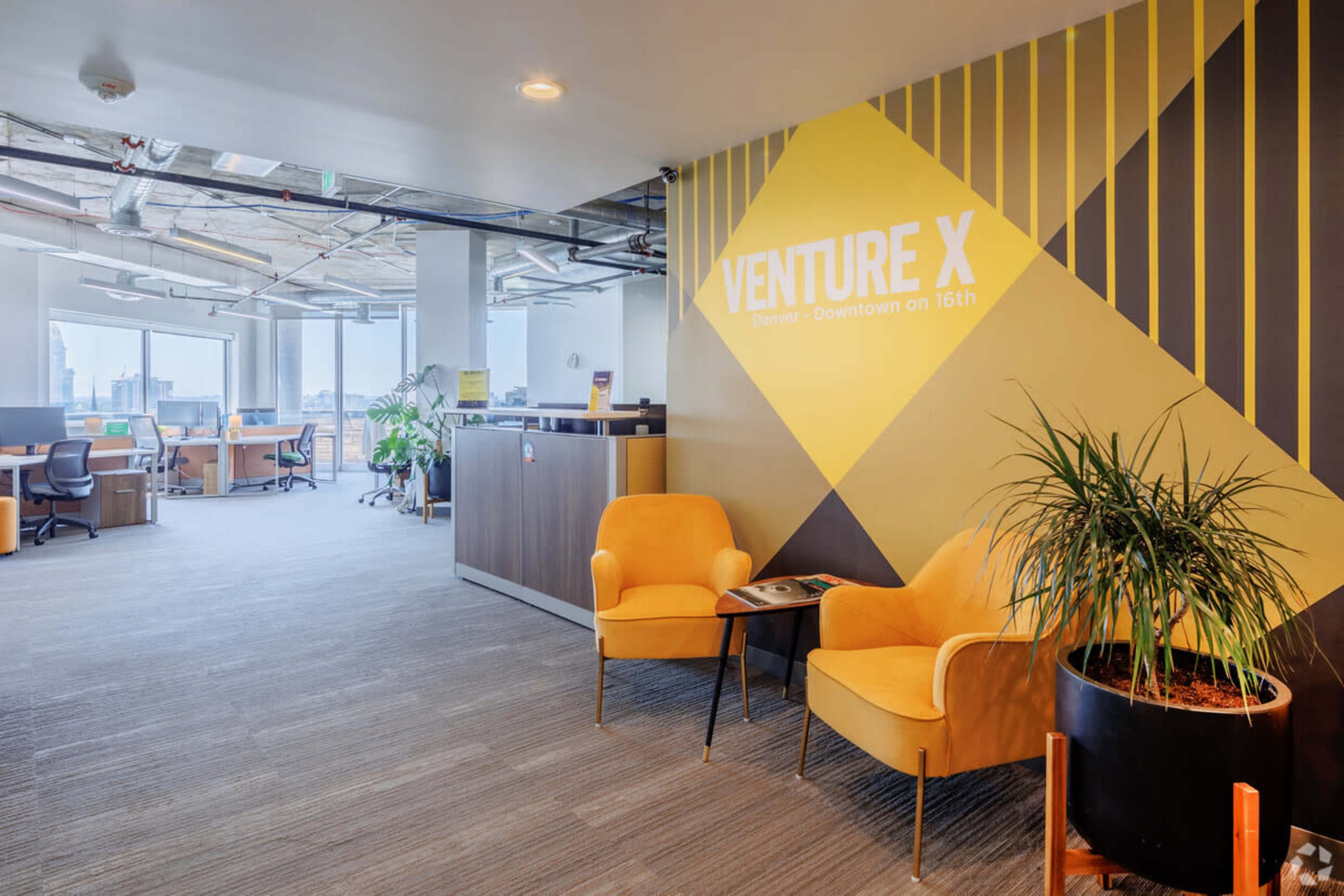 The image shows a modern office space with yellow accent chairs, a reception area, and workstations in the background under large windows.