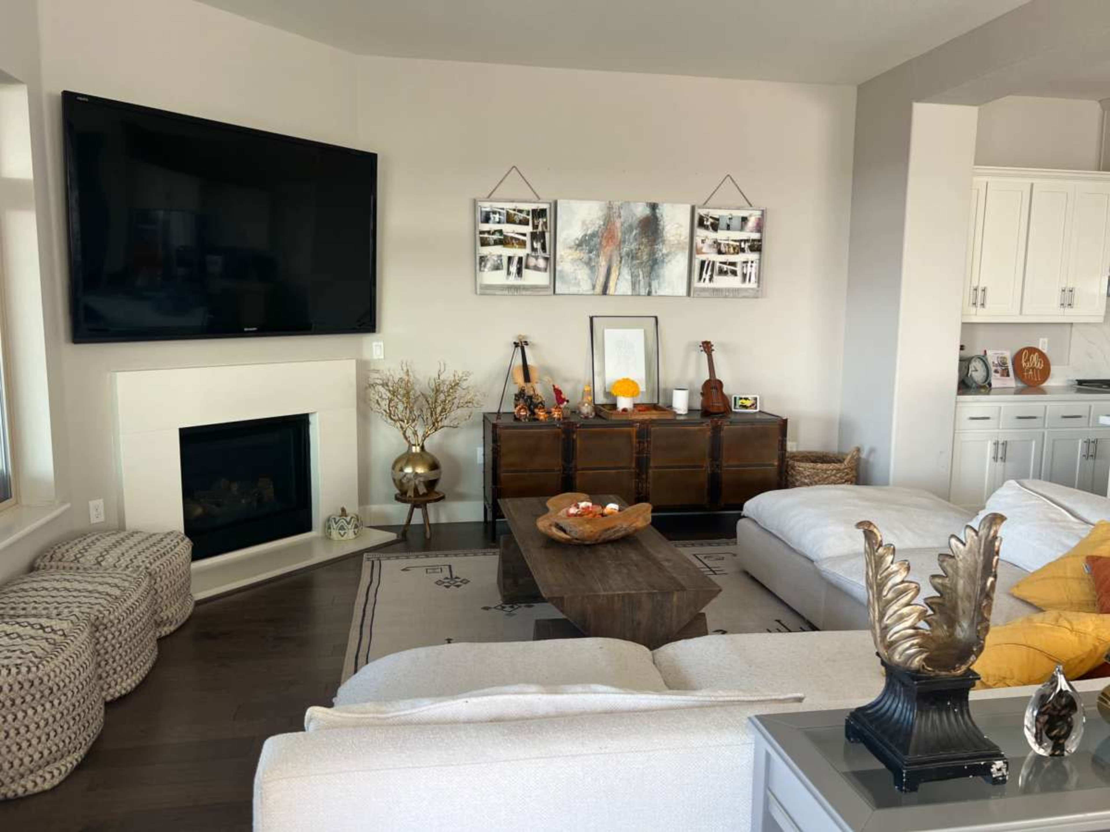 A modern living room with a large flat-screen TV mounted on the wall, a sectional sofa, a wooden coffee table, and various decorative items on display.