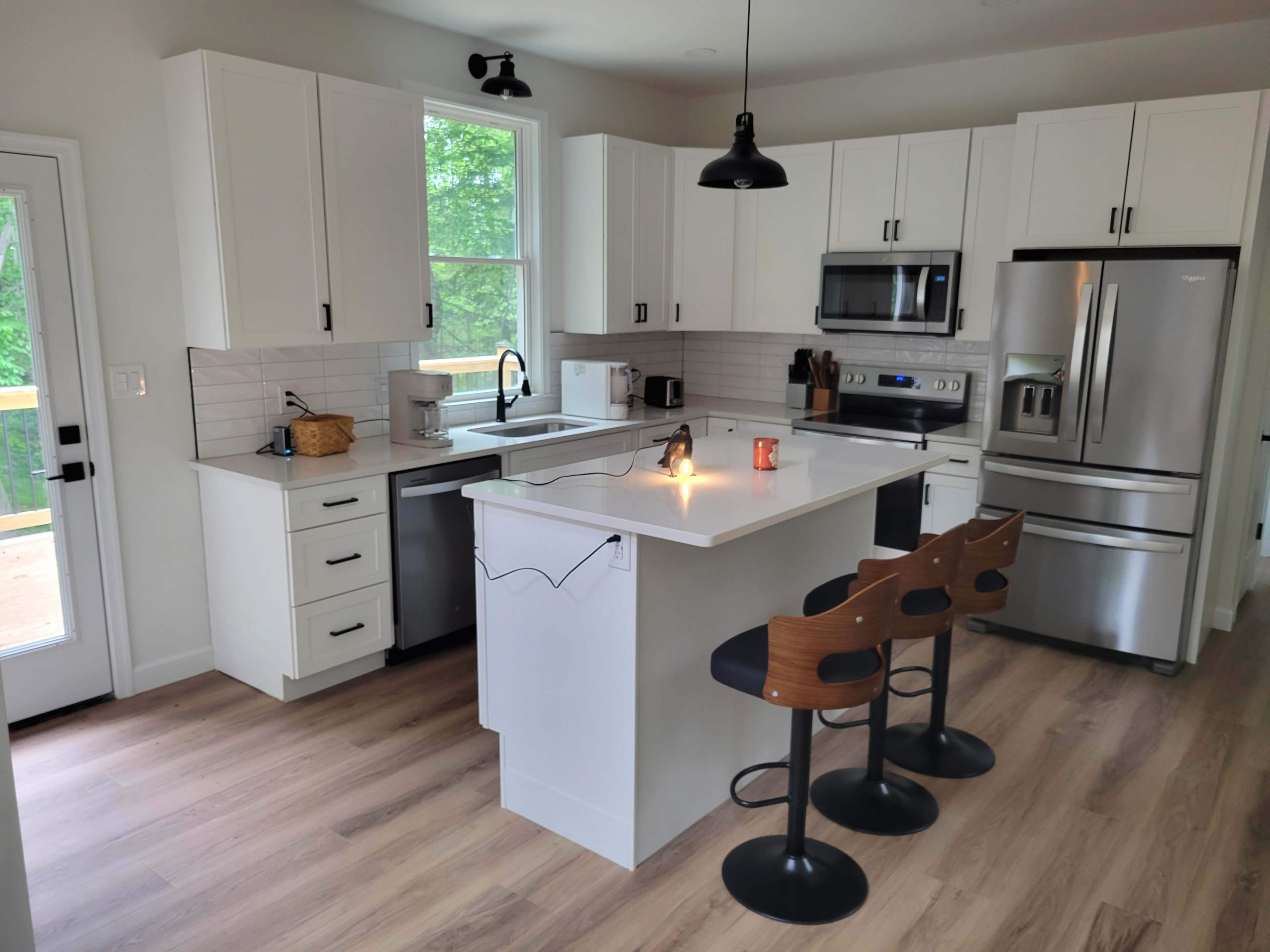 The image shows a modern kitchen with white cabinets, stainless steel appliances, and a central island with three bar stools.
