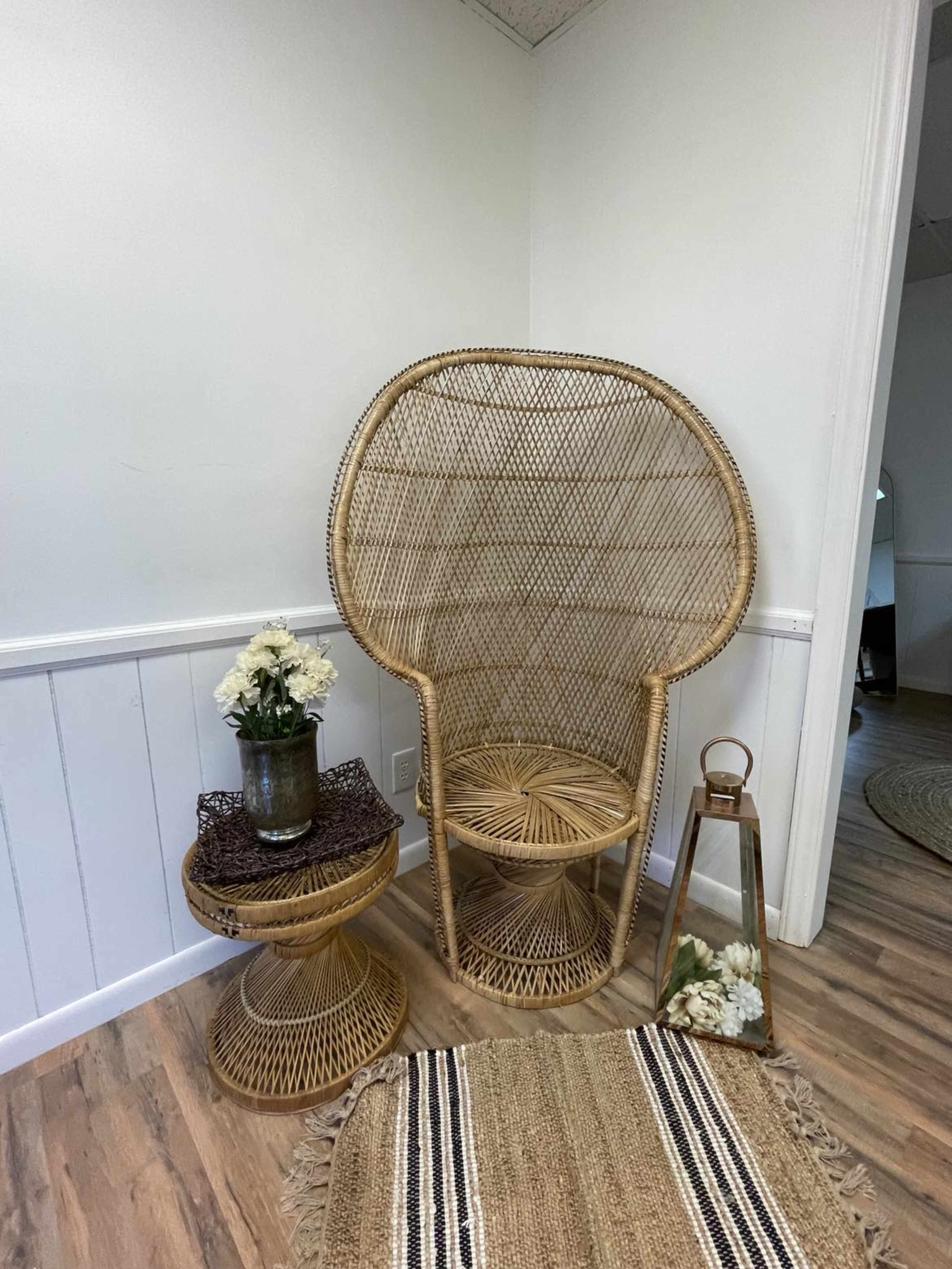 A corner setup features a rattan chair, a small round table with a vase of flowers, and a lantern on a woven rug.