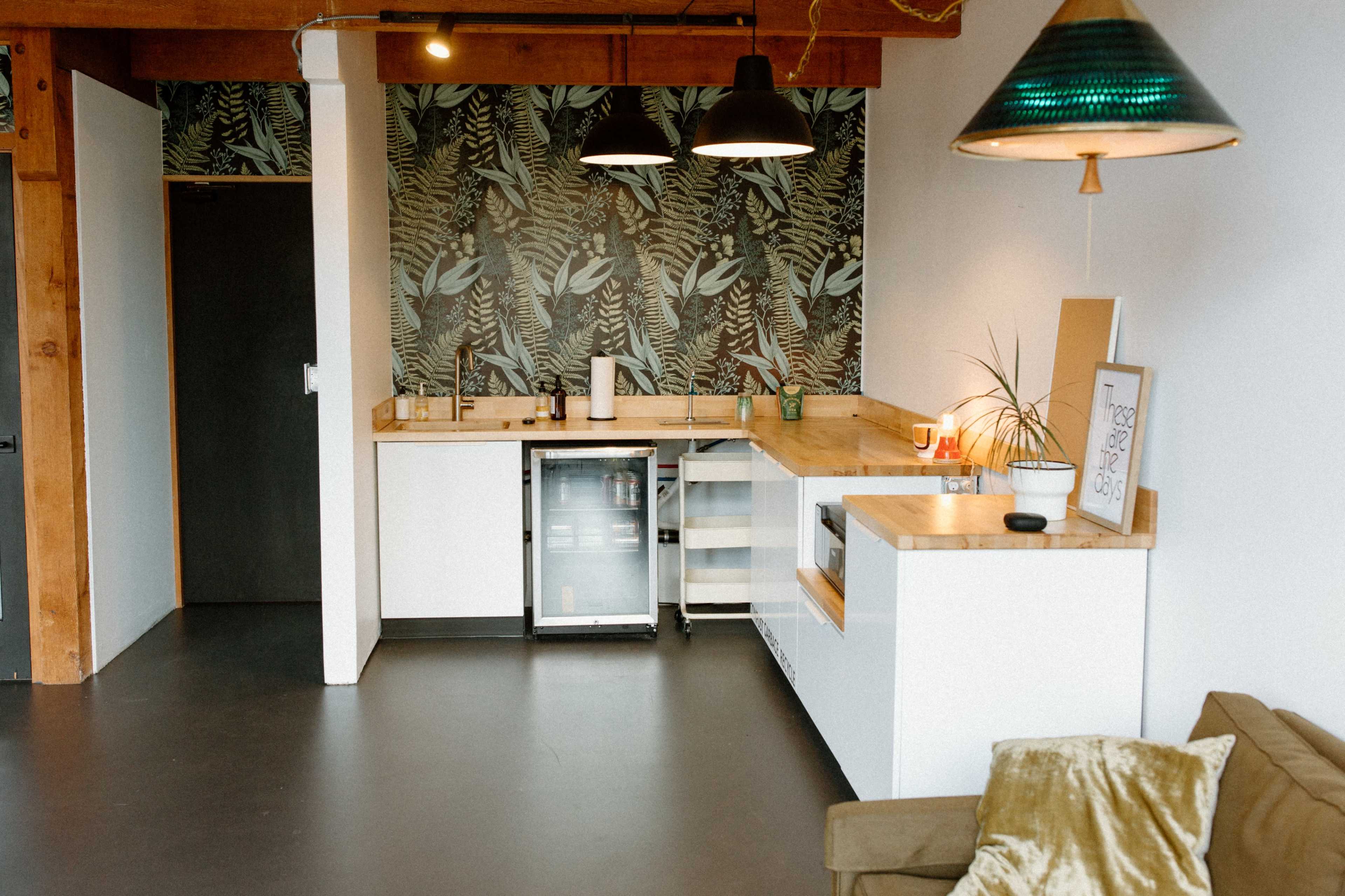 A kitchen area featuring a wooden countertop, modern fixtures, a small refrigerator, and a tropical-themed wallpaper.