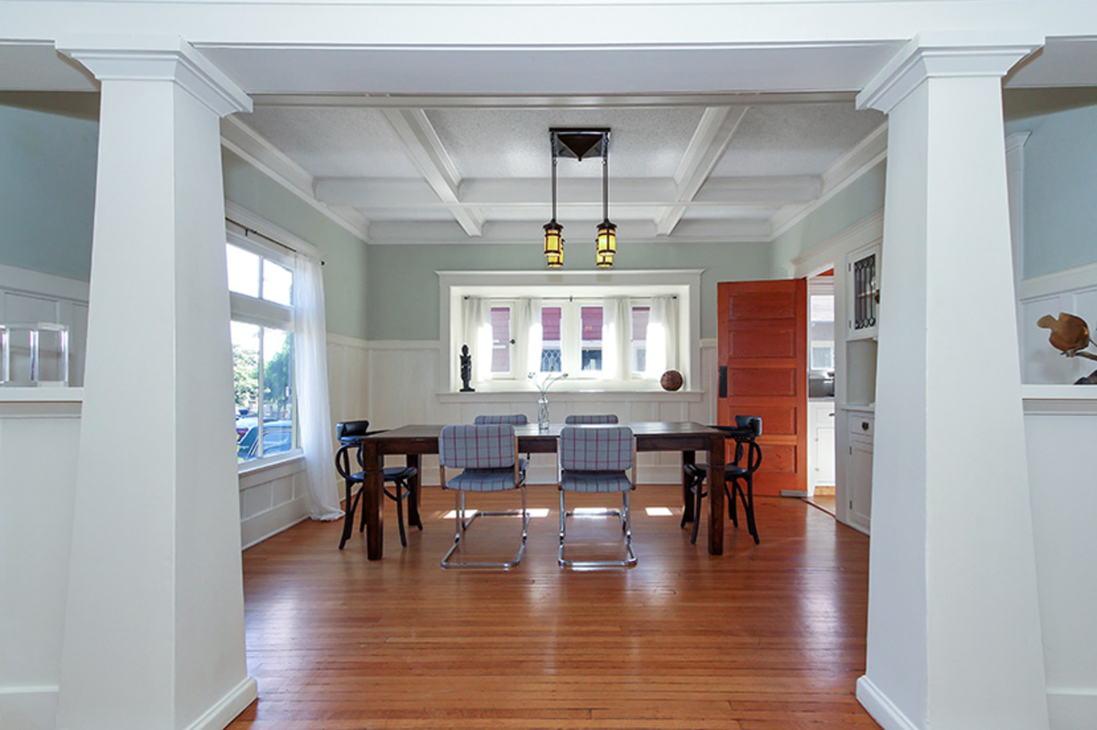 A dining room with a long table surrounded by chairs, framed by white columns and a doorway leading to another room.