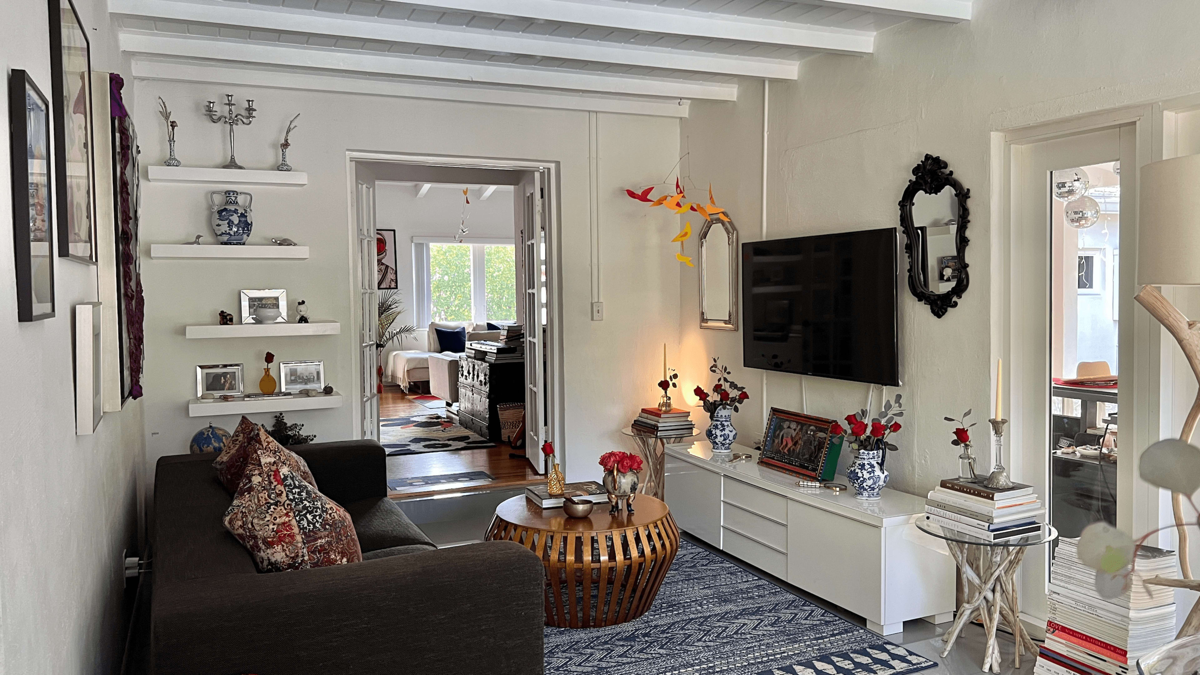 A living room with a dark sofa, a round wooden coffee table, a television mounted on the wall, and decorative items on shelves.