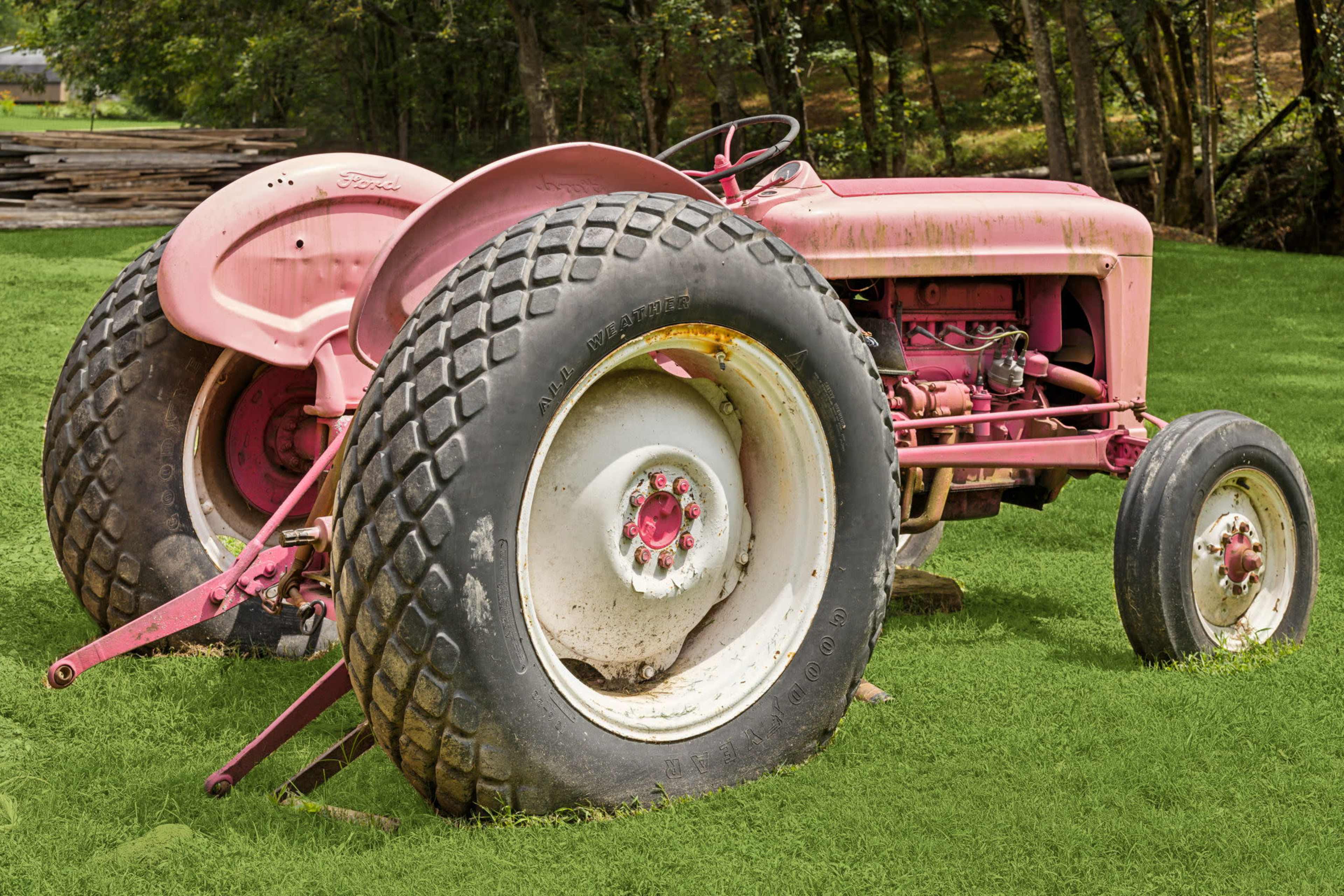 A pink Ford tractor is parked on a grassy area surrounded by trees.