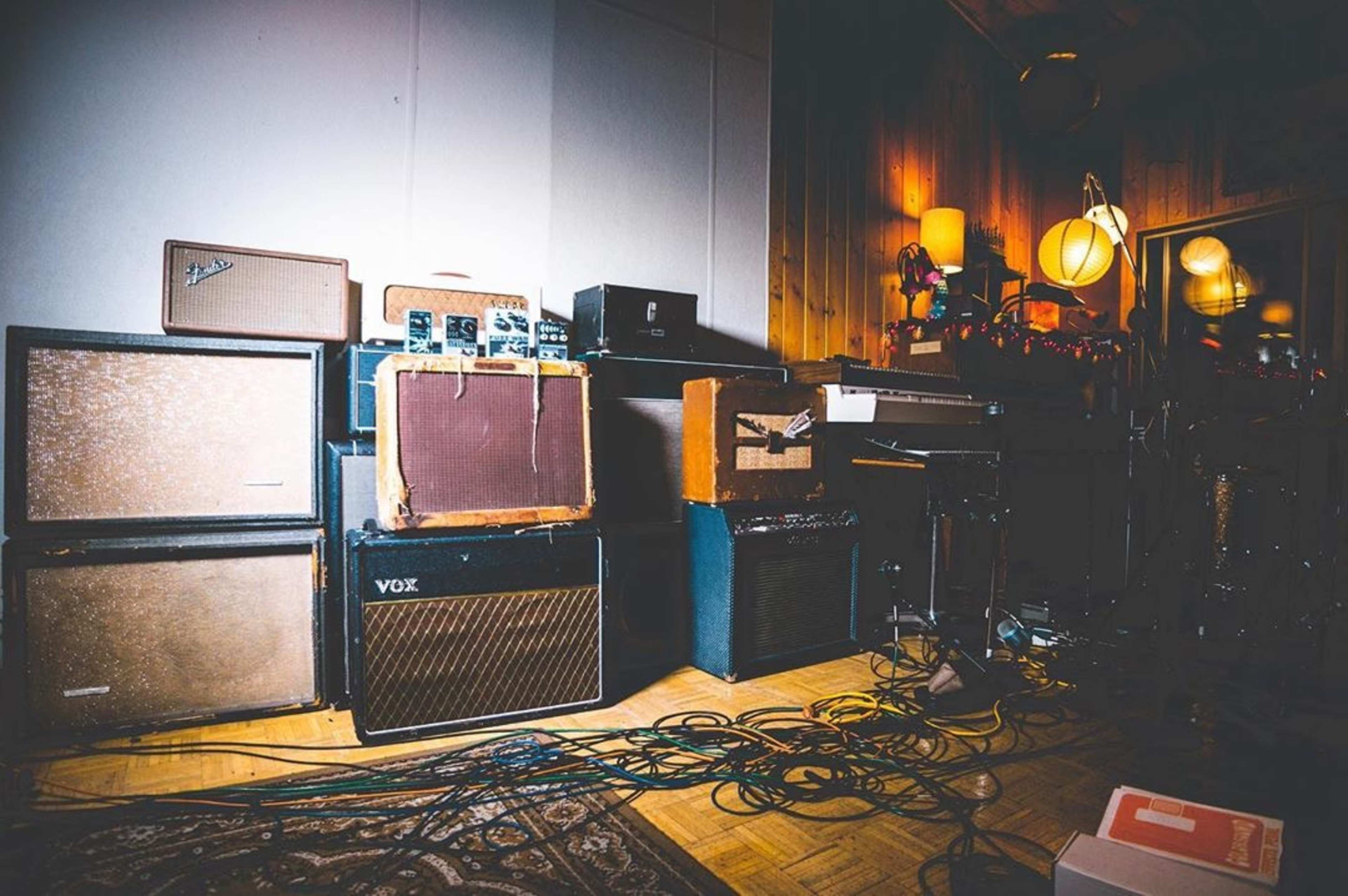 A collection of vintage guitar amplifiers stacked against a wall in a music studio, with cables and a rug on the floor.