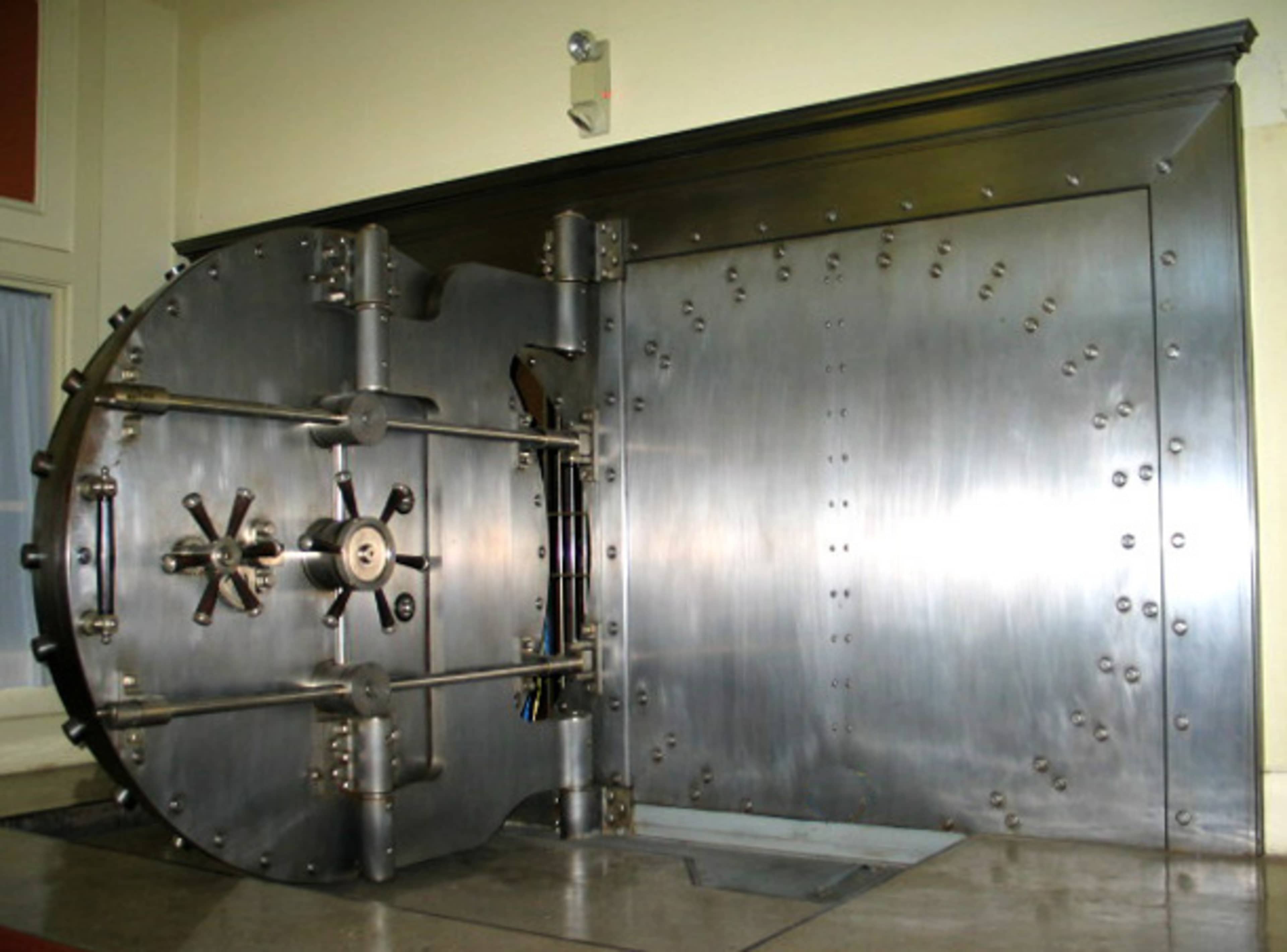 A large, industrial vault door made of polished metal, opened to reveal the interior of the vault.