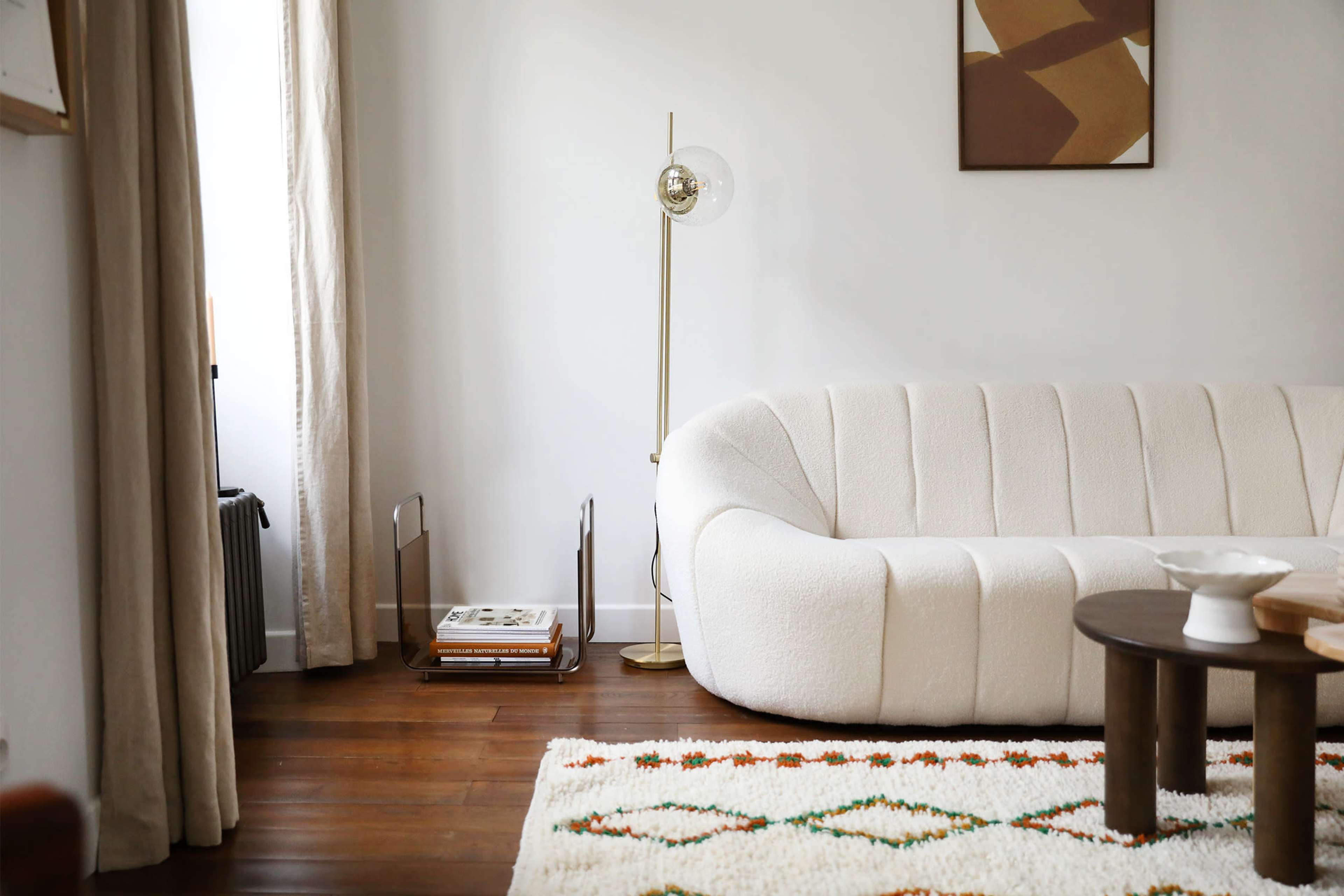 A modern living room featuring a curved white sofa, a wooden coffee table, a floor lamp, and a textured area rug.