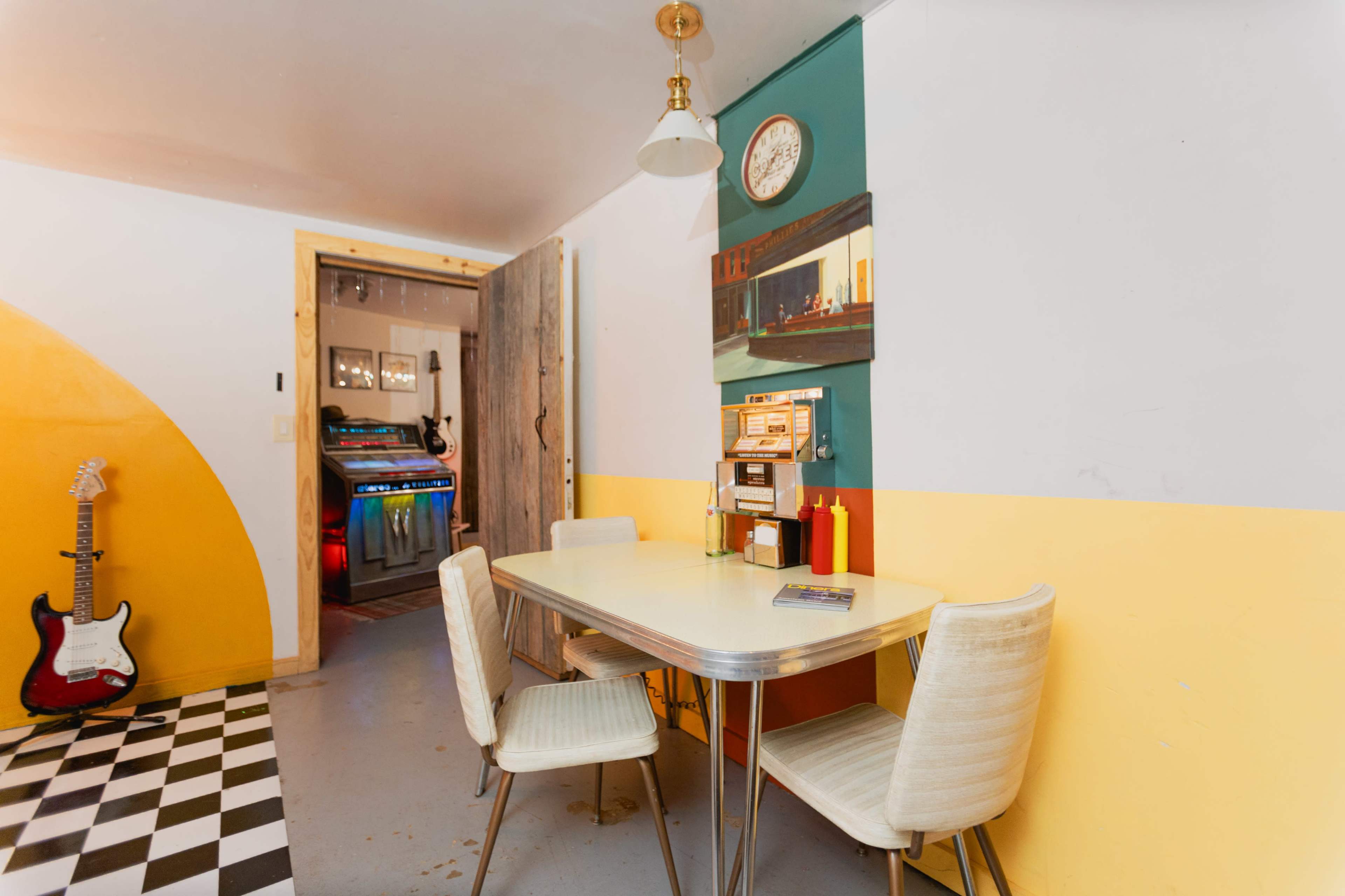 A retro-style dining table with two chairs is situated in a room with yellow and white walls, while a vintage jukebox can be seen in the background.