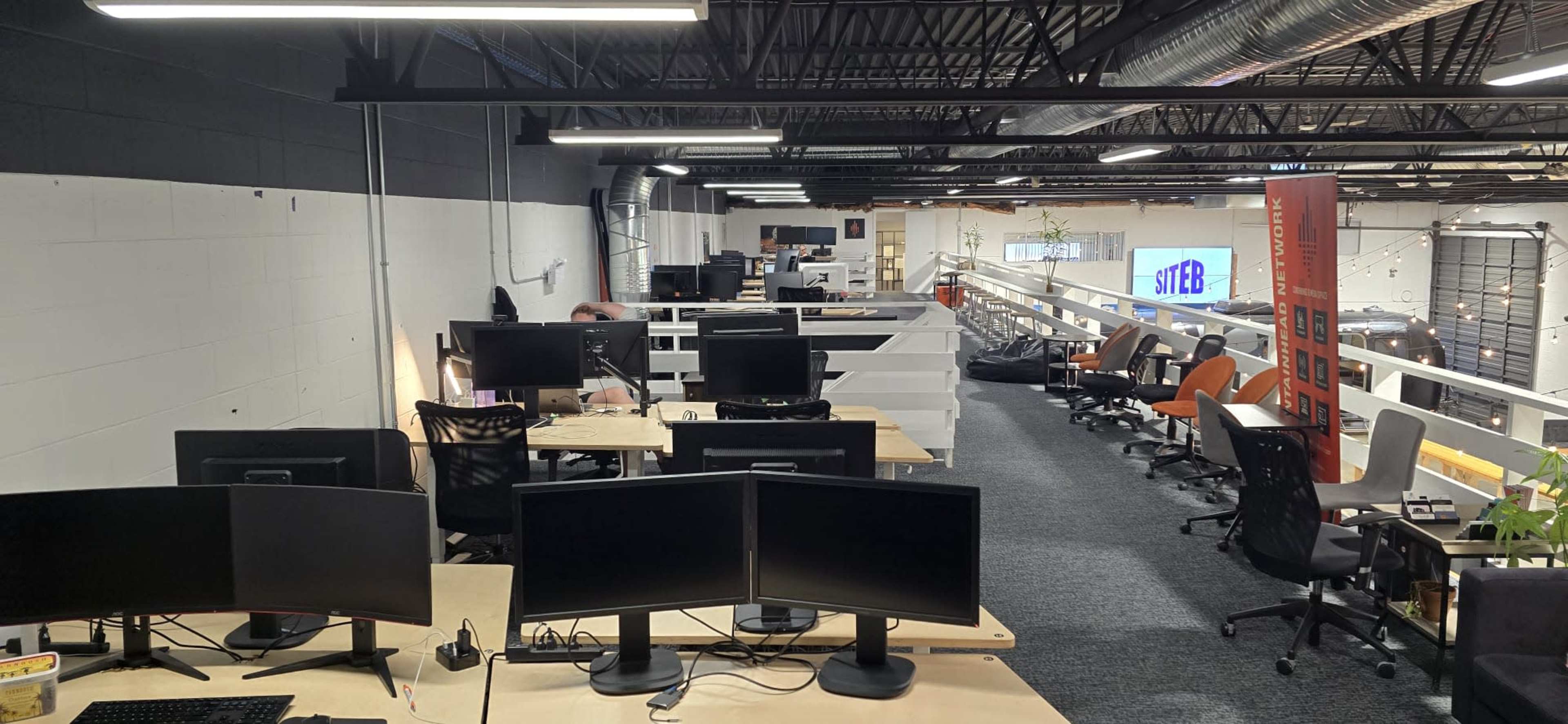An open office space with multiple desks equipped with computer monitors and ergonomic chairs, featuring a modern design and bright lighting.