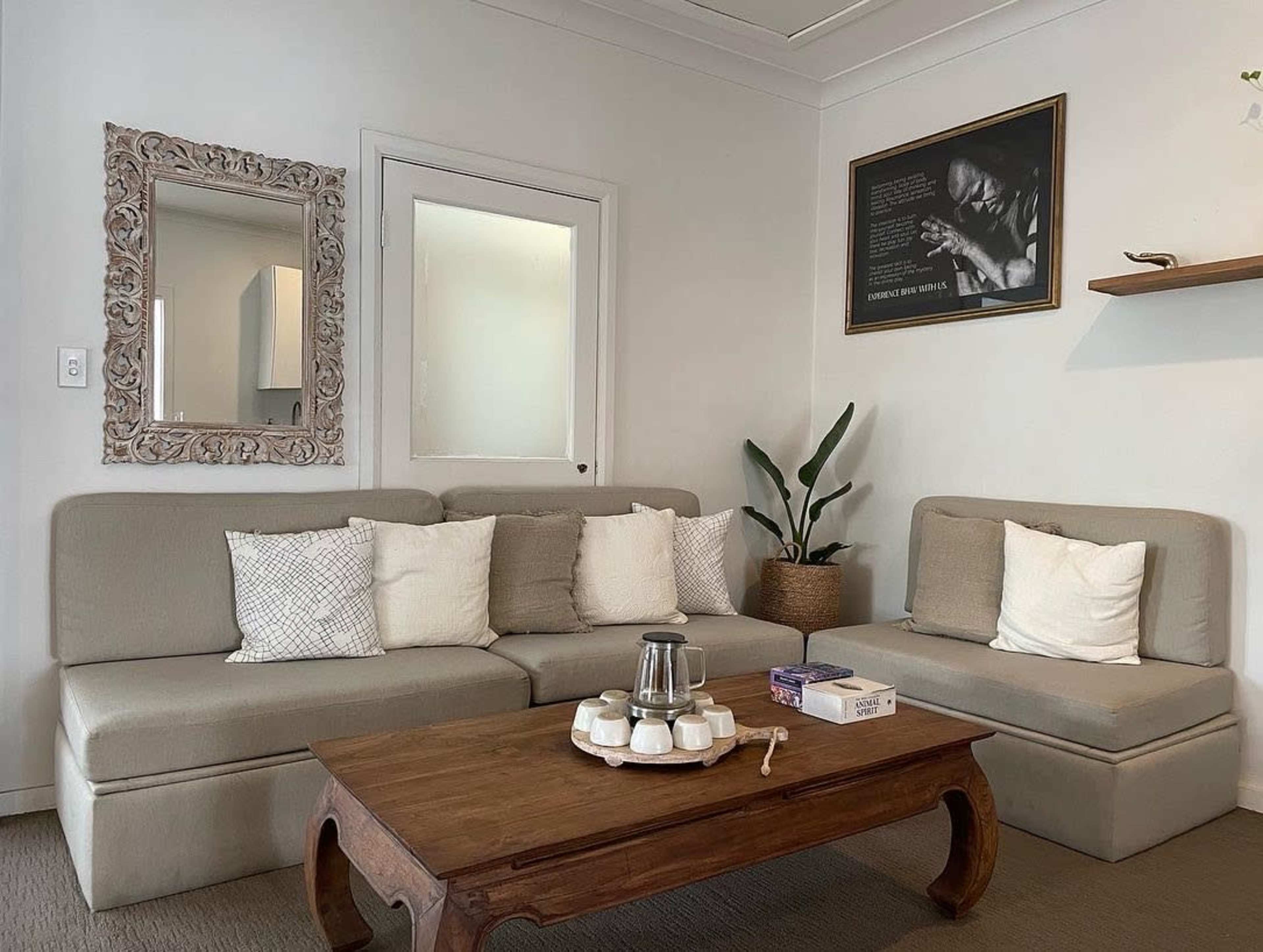 A cozy living room with a beige sectional sofa, a wooden coffee table, and a decorative mirror on the wall.
