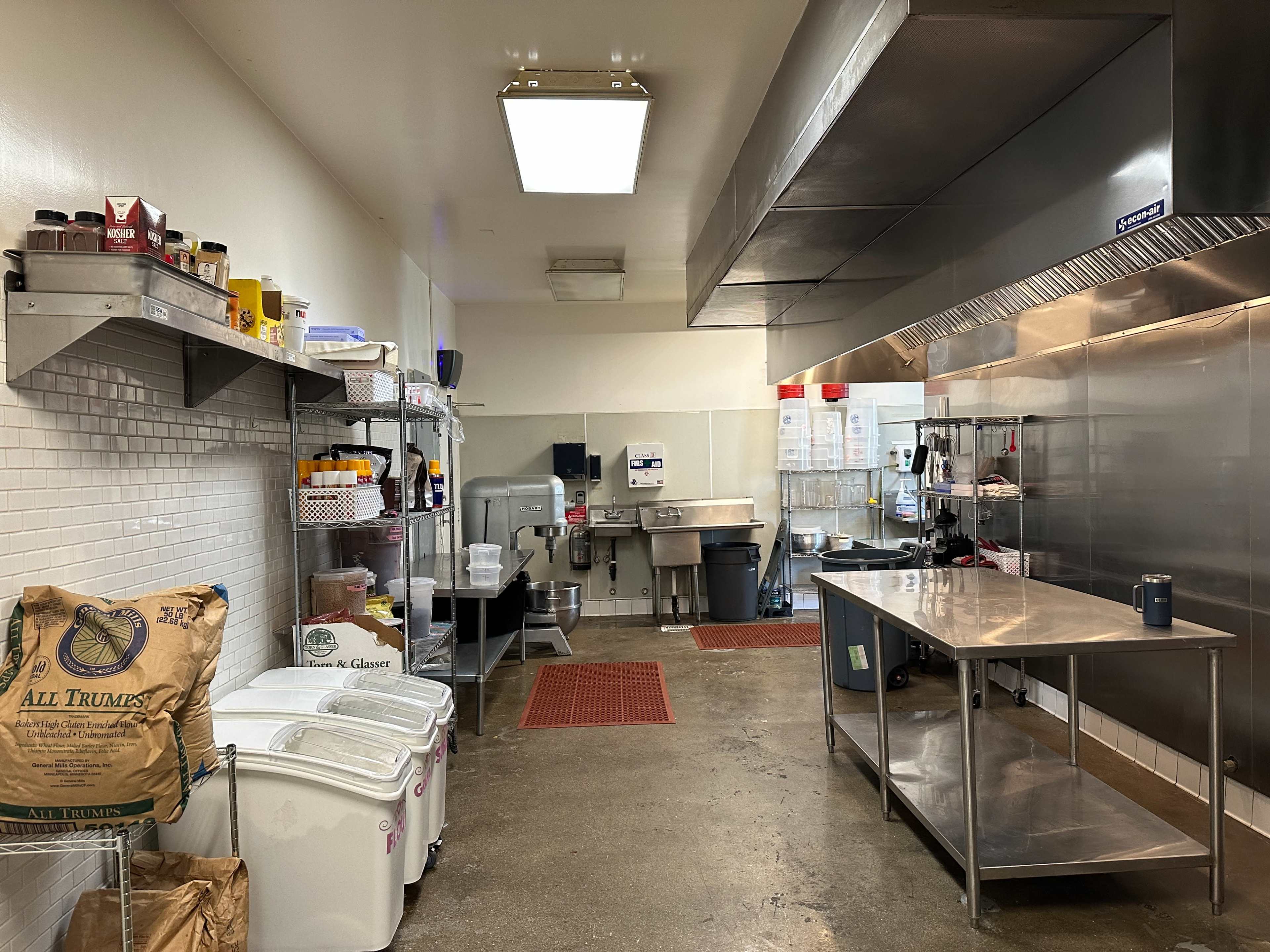 A commercial kitchen with stainless steel equipment, shelves stocked with condiments, and a clean floor.