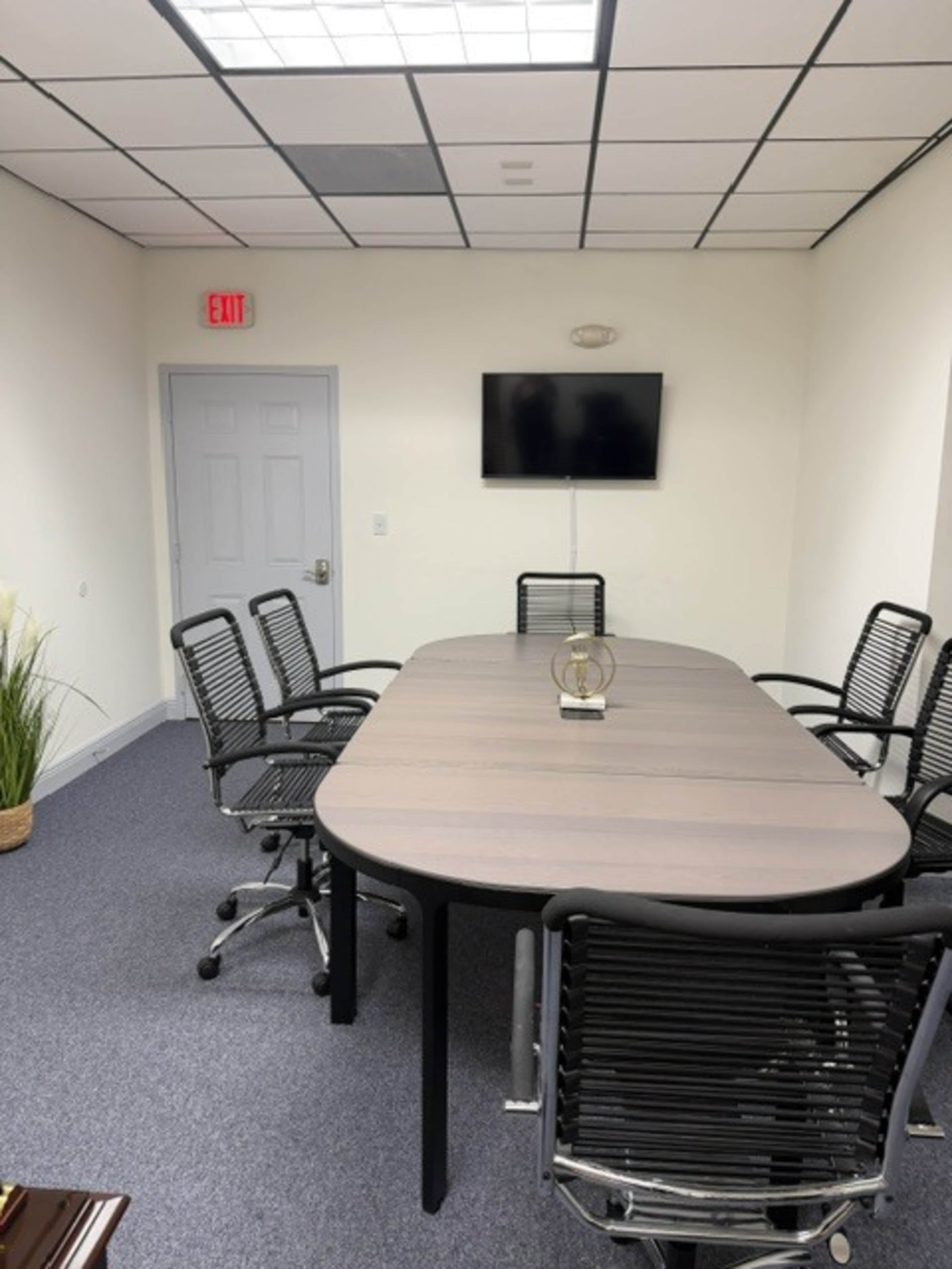 A conference room features a large oval table surrounded by six black mesh chairs and a wall-mounted television.