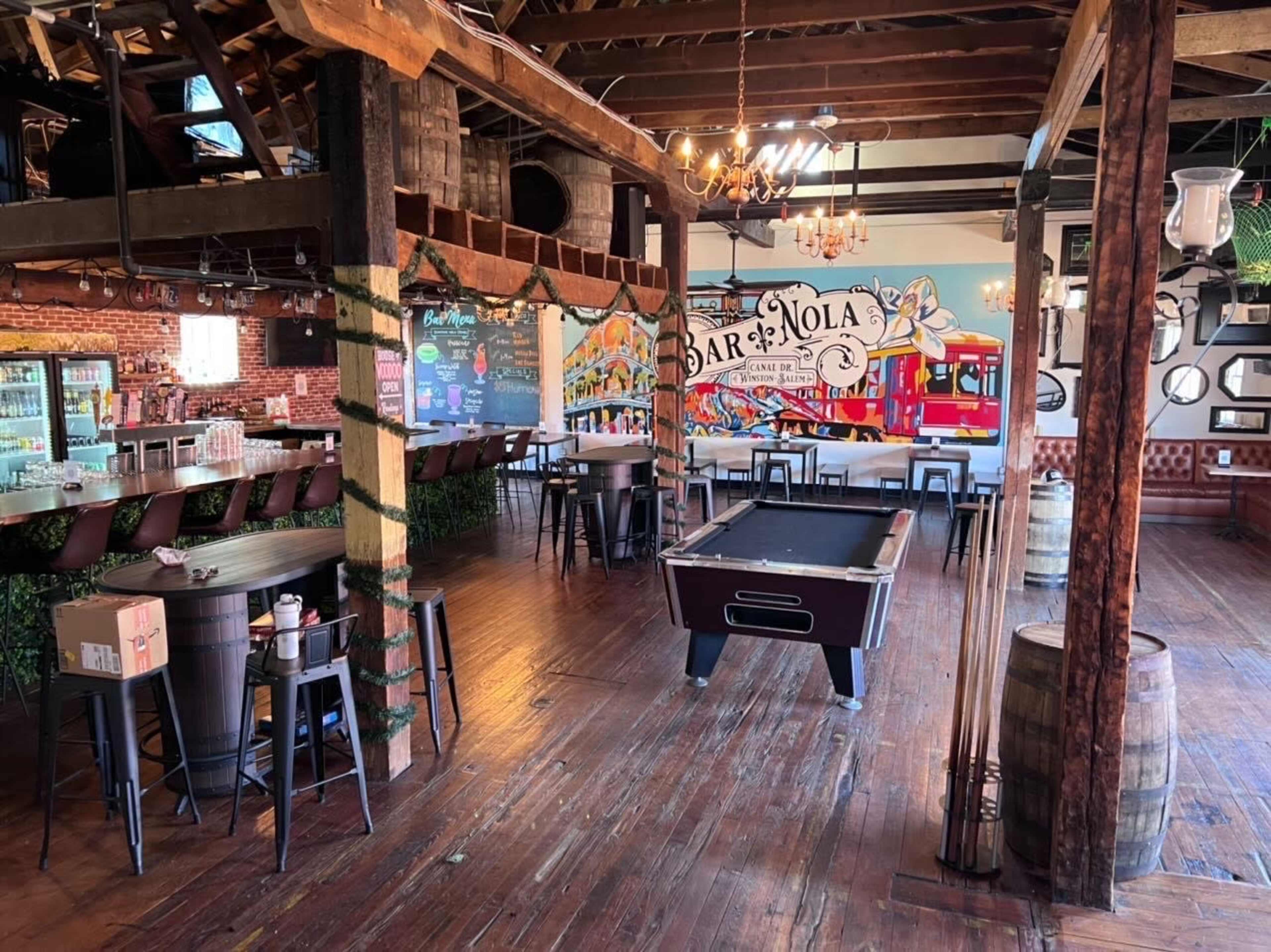 A lively bar interior featuring a pool table, a long wooden bar, and colorful murals on the walls.