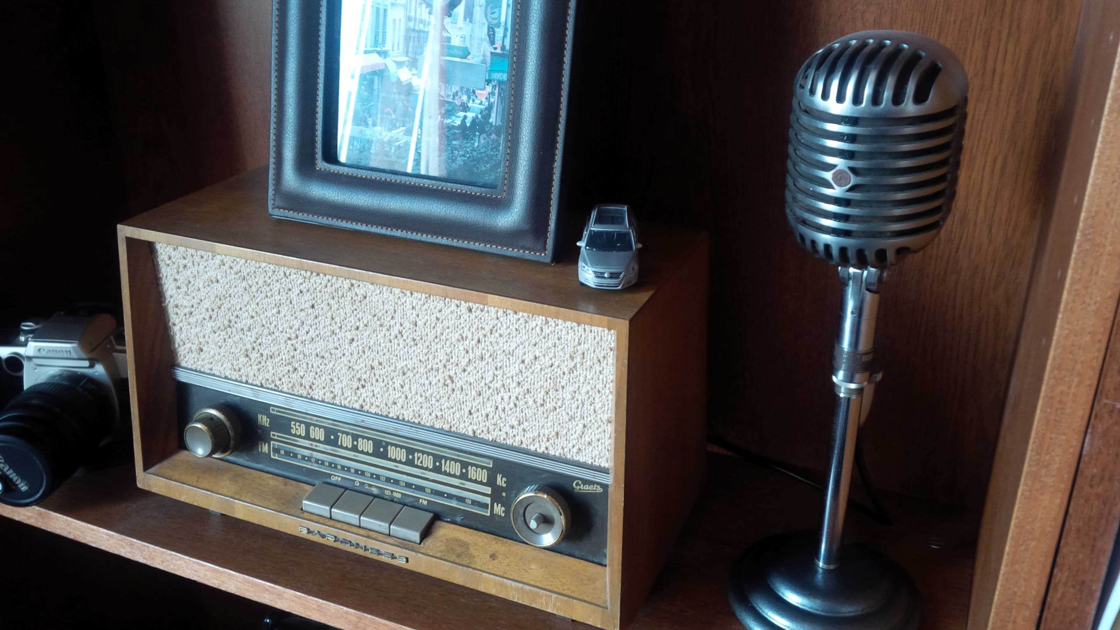 A vintage radio sits on a shelf alongside a framed photograph, a small toy car, and a classic microphone.