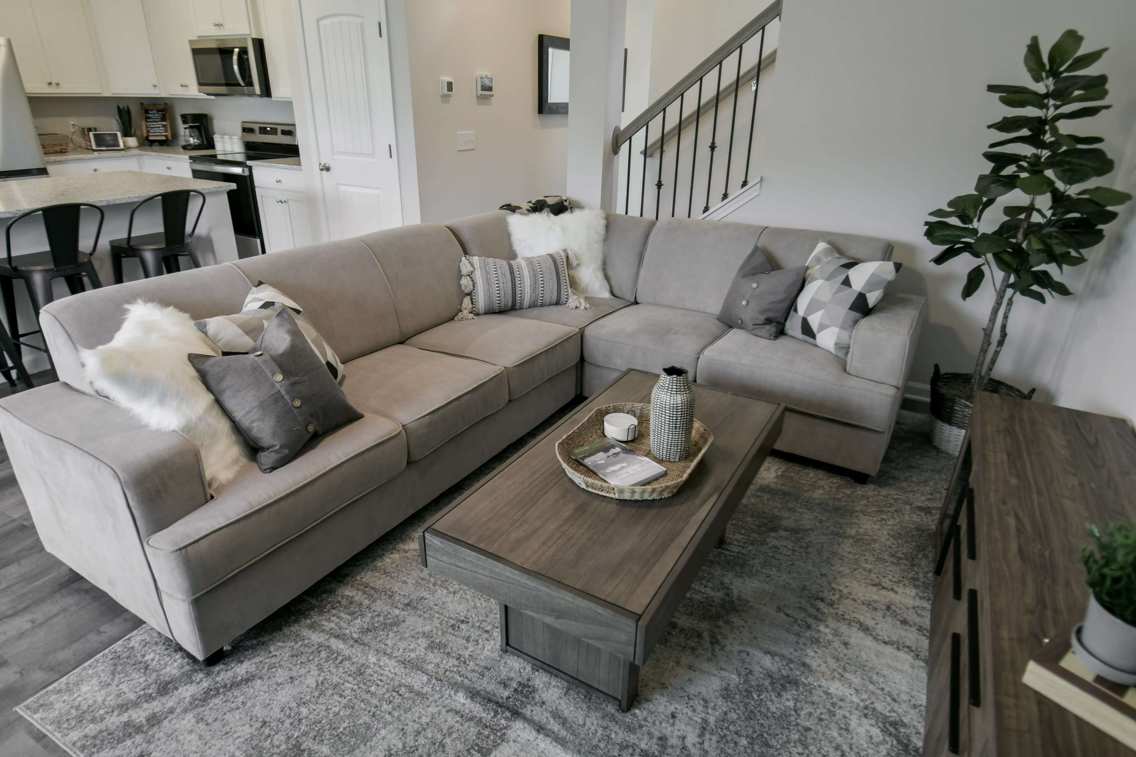 A modern living room featuring a grey sectional sofa adorned with decorative pillows, a wooden coffee table with decorative items, and a plant in the corner.