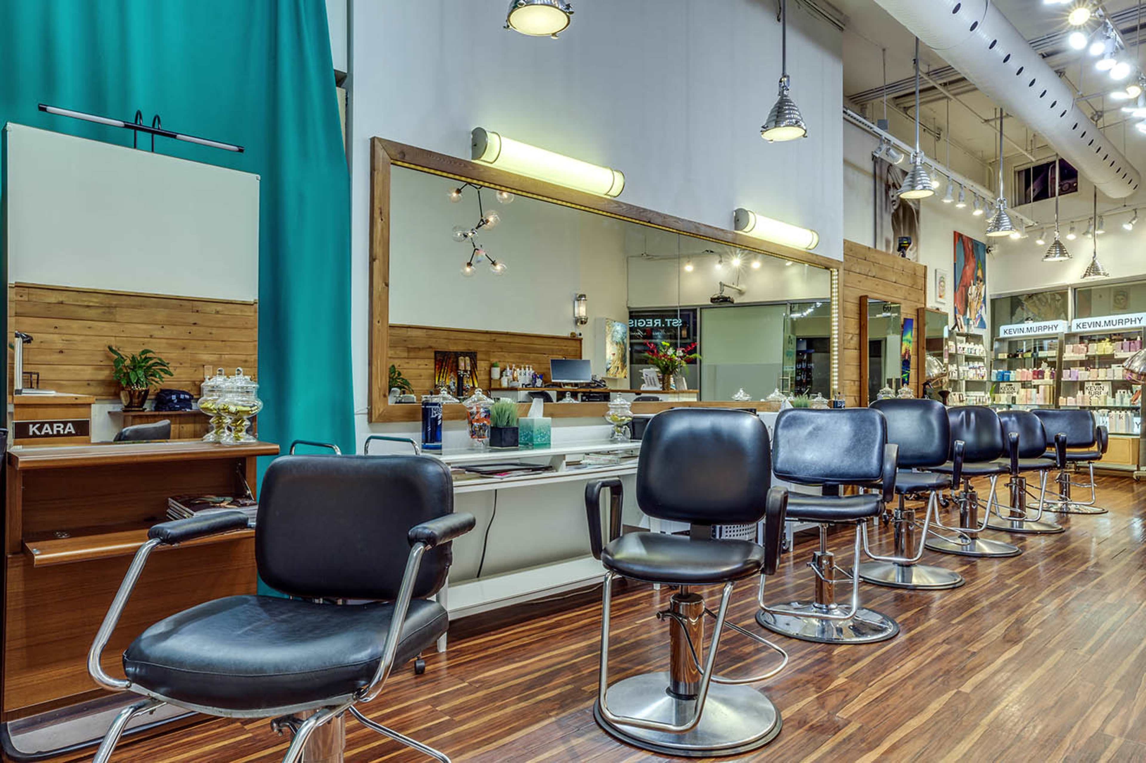 A modern hair salon interior with several black styling chairs, a large mirror, and shelves stocked with hair products.