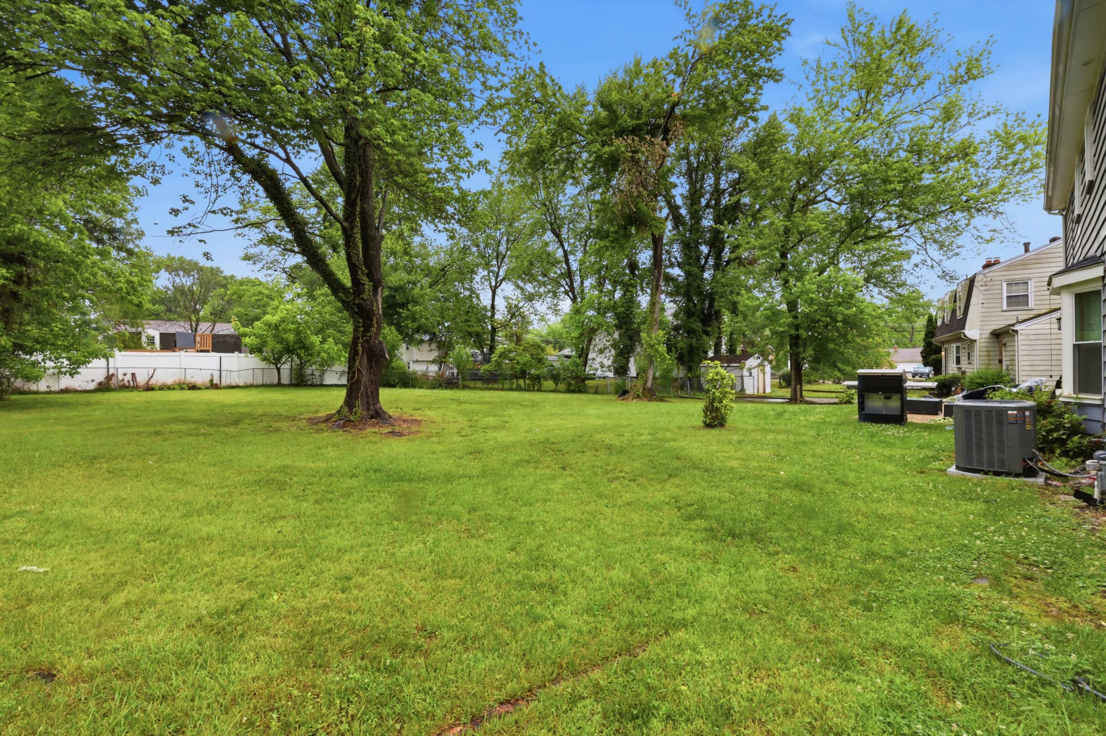 The image shows a spacious green backyard with several trees and a few garden structures in the distance.