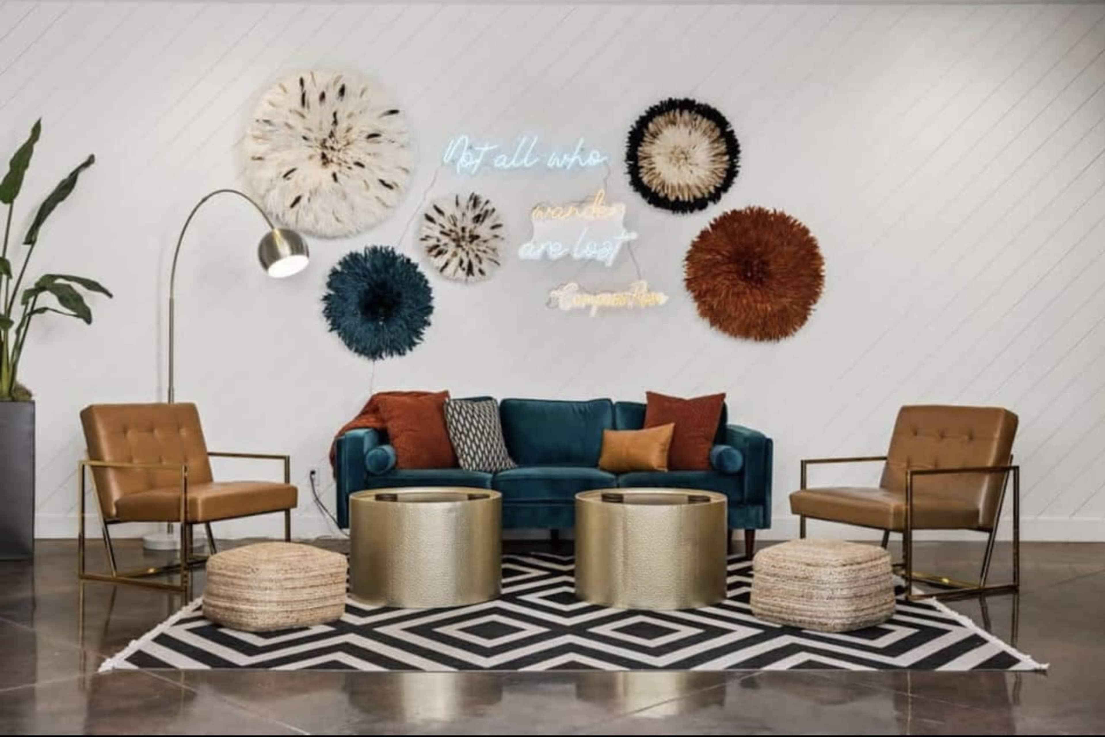 A modern living room features a blue velvet sofa, gold-accented chairs, round metallic coffee tables, and decorative wall art, all set against a patterned rug.