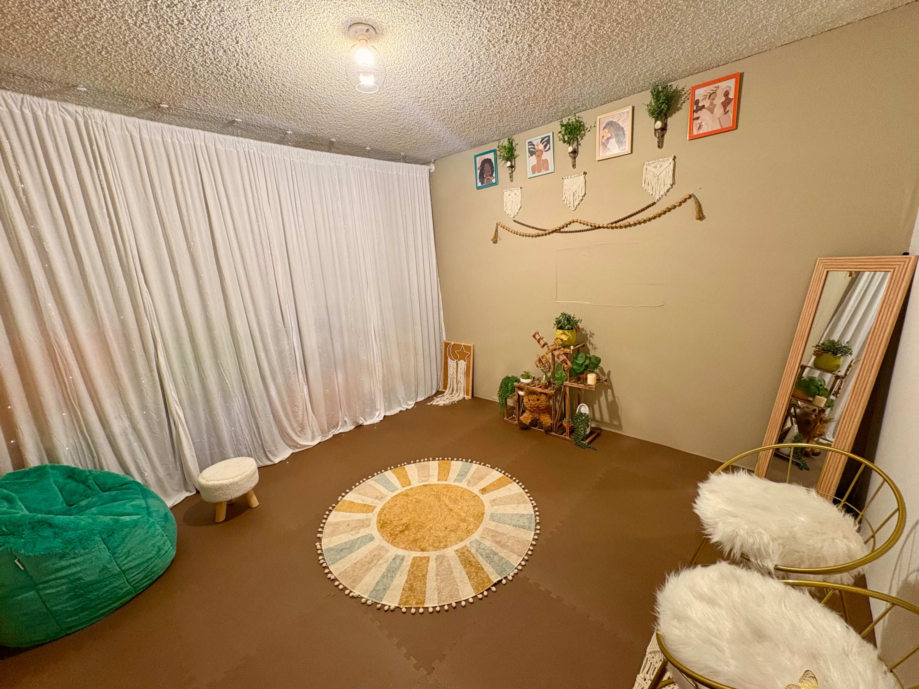 The image shows a cozy, minimalistic room with a round area rug, a bean bag chair, a mirror, and decorated walls featuring framed artwork.